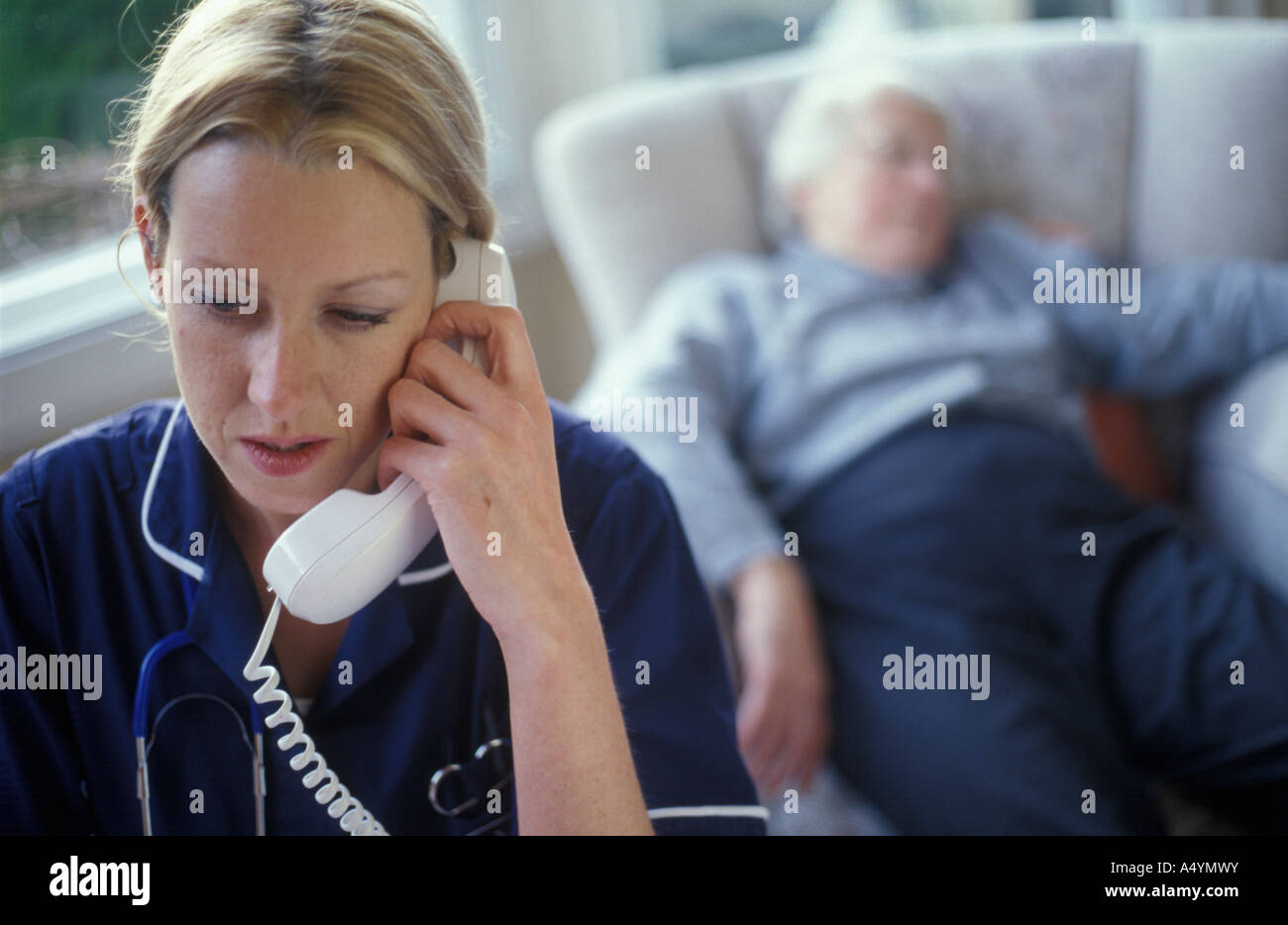 district nurse on the telephone with elder lady collapsed in the background Stock Photo