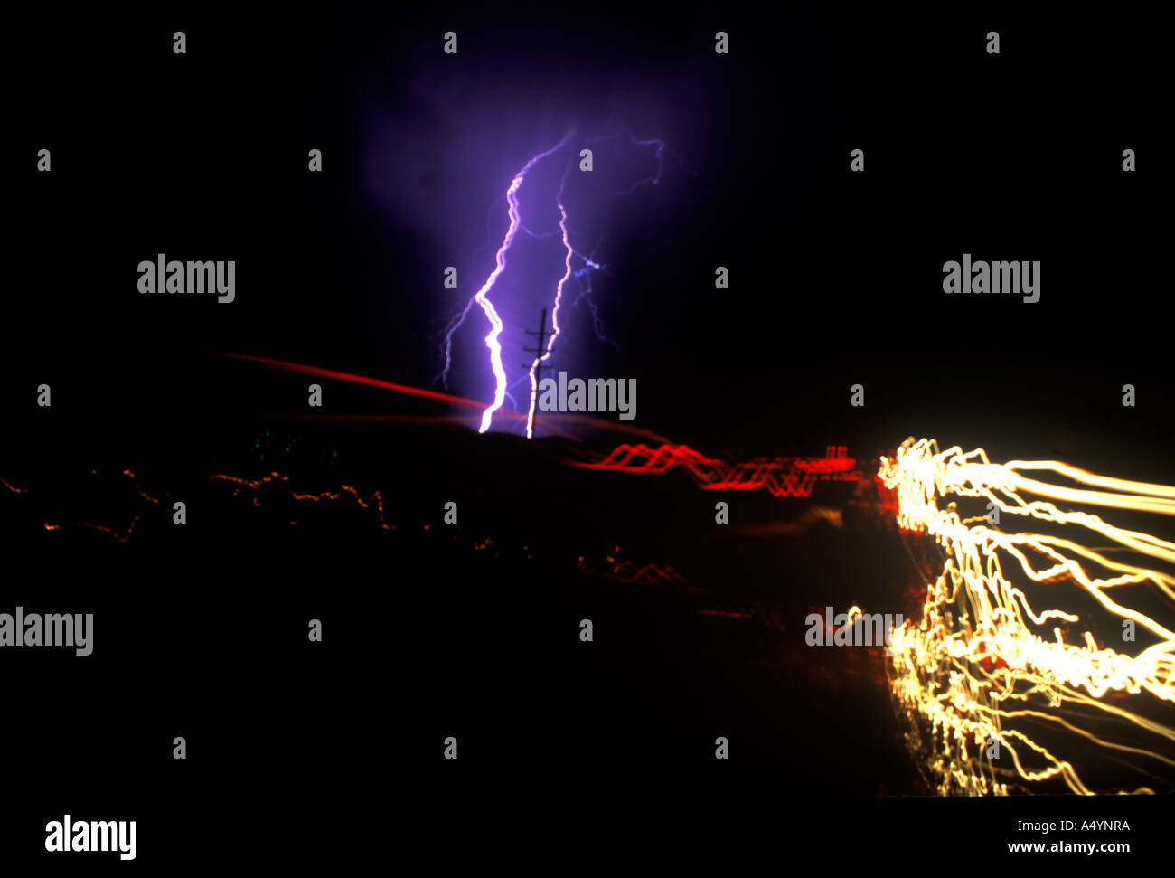 Lightning bolts strike down on a power pole with blurry car lights streaking the foreground. Stock Photo