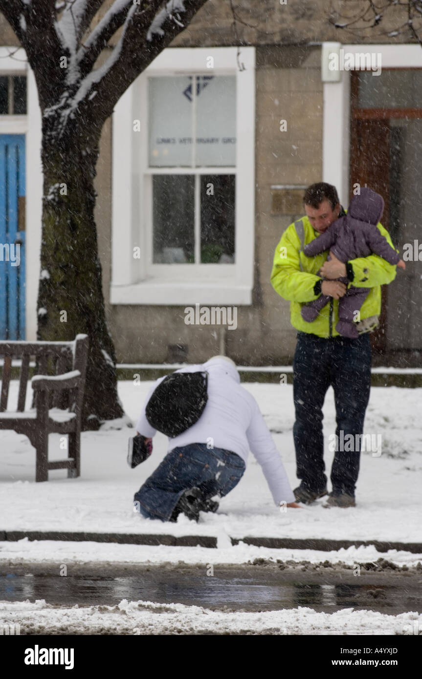 Lady after a fall on the pavement in heavy snow, while being watched by her family Stock Photo