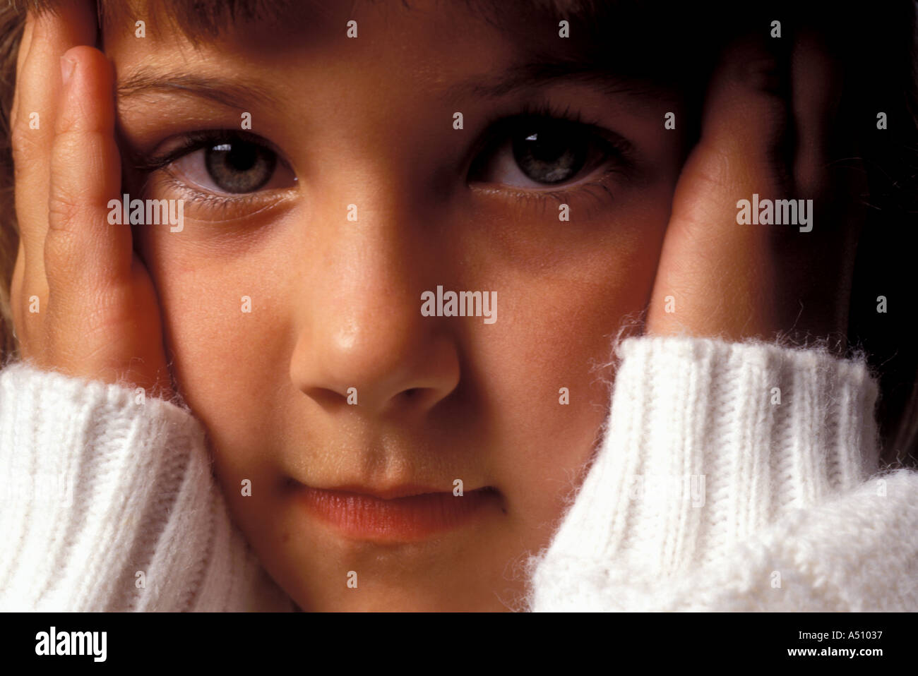 Young blond girl in white sweater holding her hands on either side of her face Stock Photo