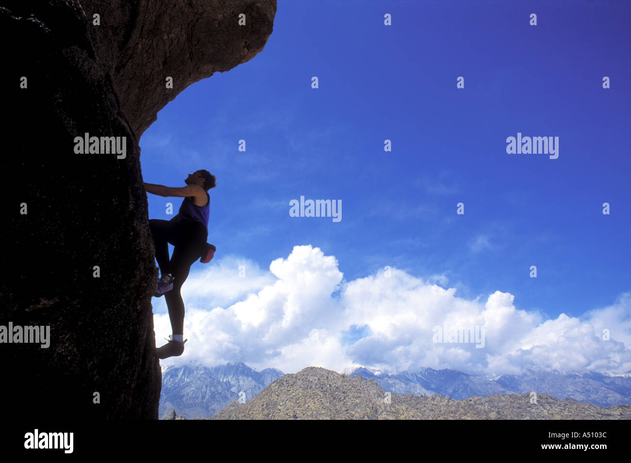 Silhouette of lone man rock climbing up vertical surface Stock Photo