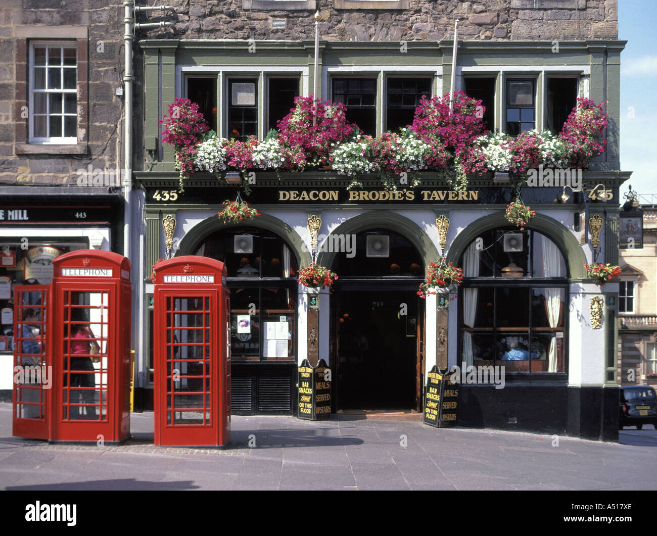 Public house Deacon Brodie Tavern with traditional iconic red phone boxes and summer flower display Lawnmarket Edinburgh Old Town Scotland UK Stock Photo