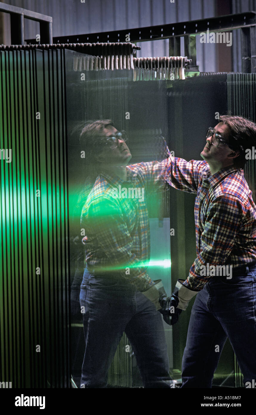 worker handling heavy glass sheet in window manufacturing plant Stock