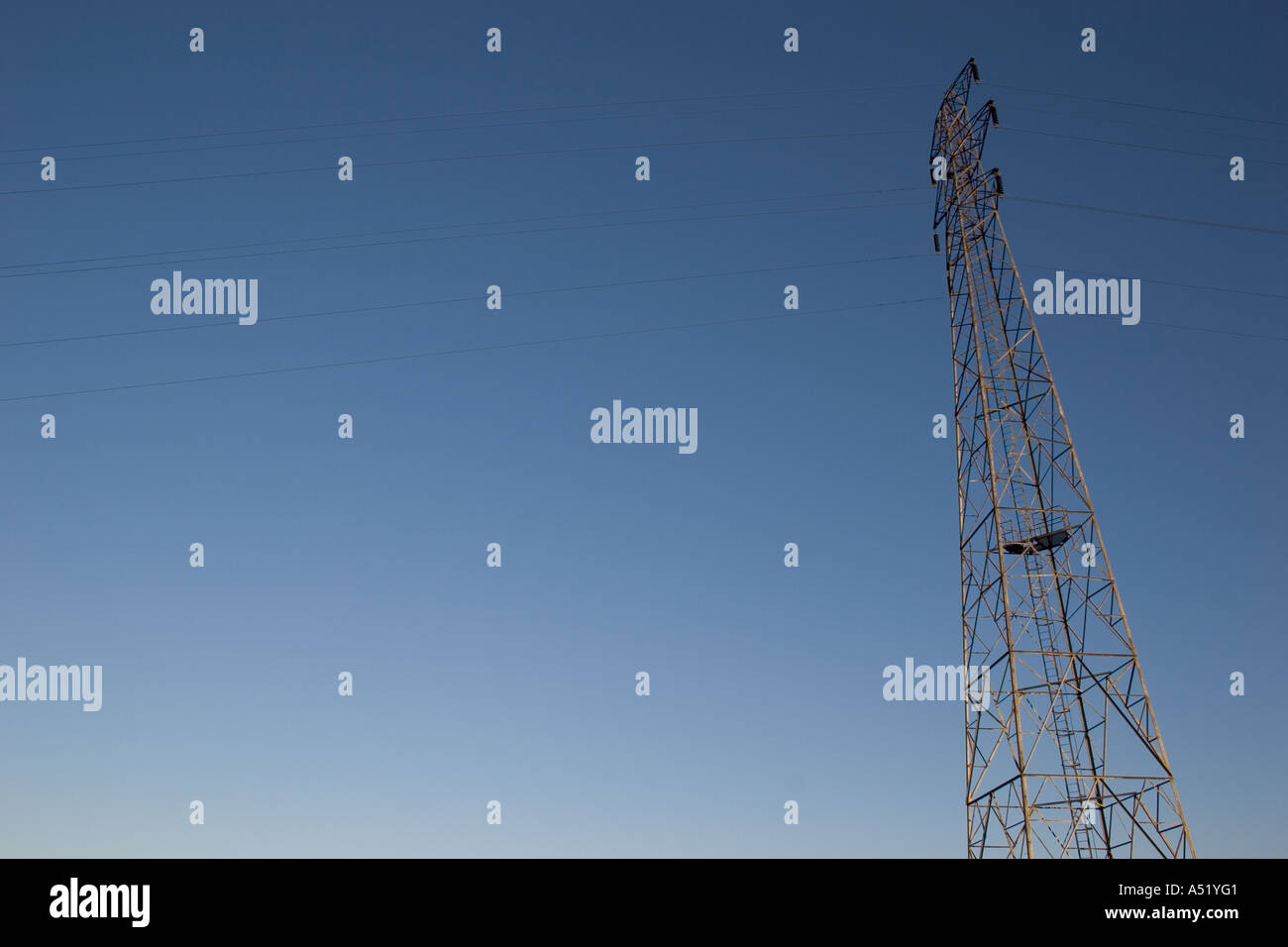Tall electricity pylon against a plain blue sky Stock Photo - Alamy