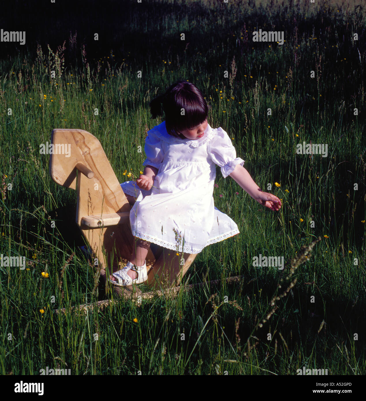 girl in white dress sitting on a horselike wooden rocking chair. Photo