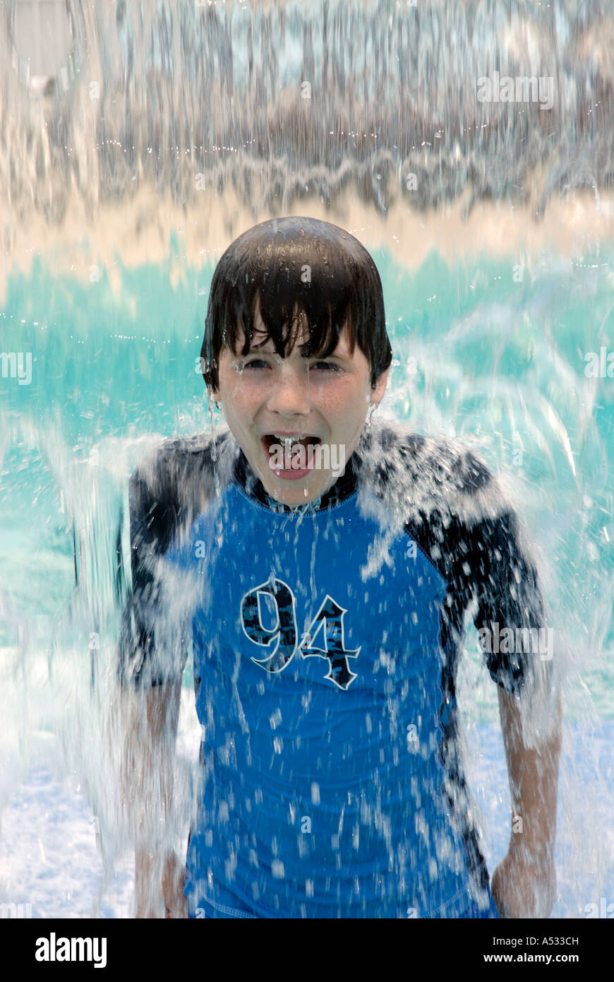 Young boy smiling in water fall waterfall cooling off at playground in summer.  Properties of water.  Water is a powerful evapor Stock Photo