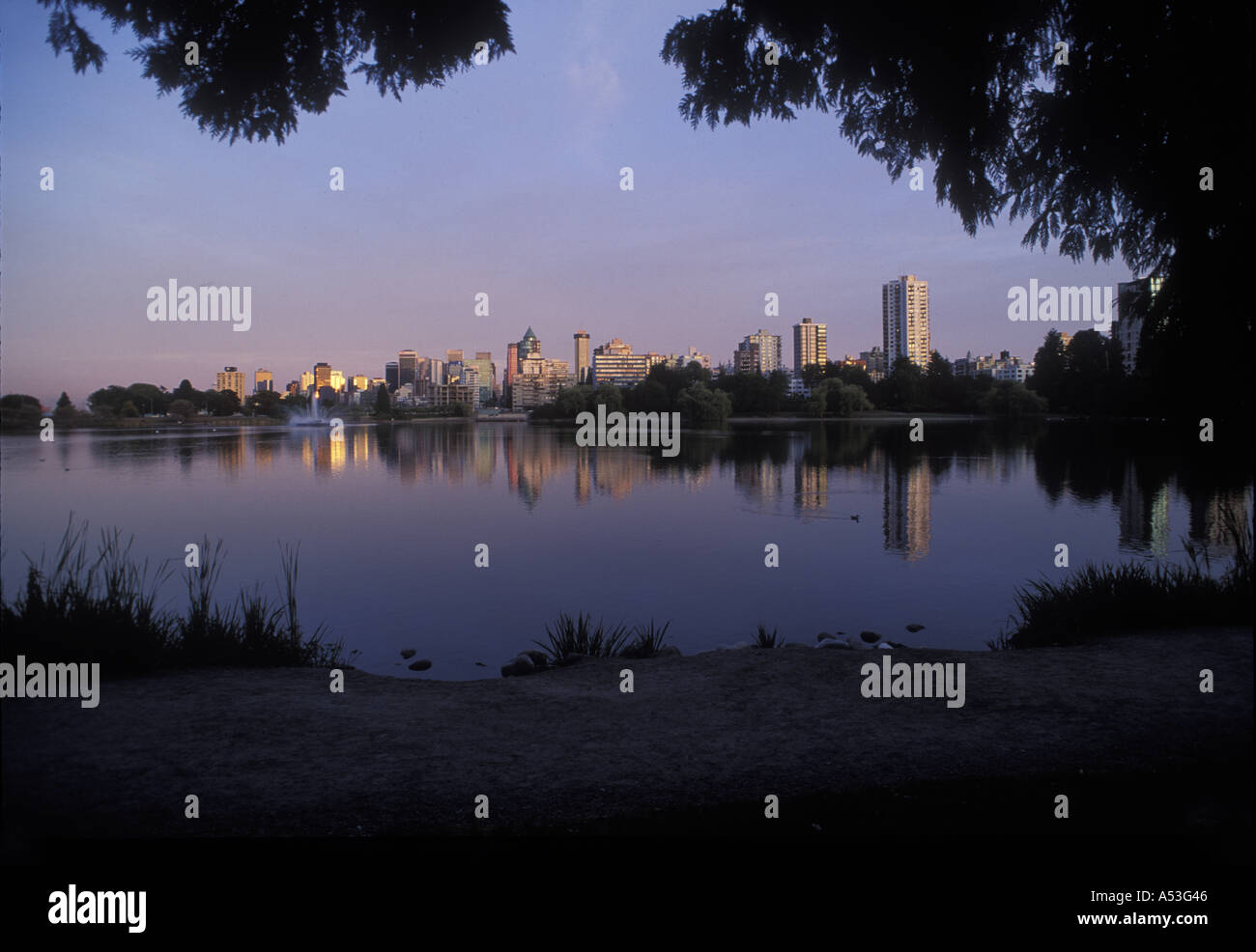 Canada British Columbia Vancouver City skyline viewed from Stanley Park at sunset along Lost Lagoon on summer evening Stock Photo