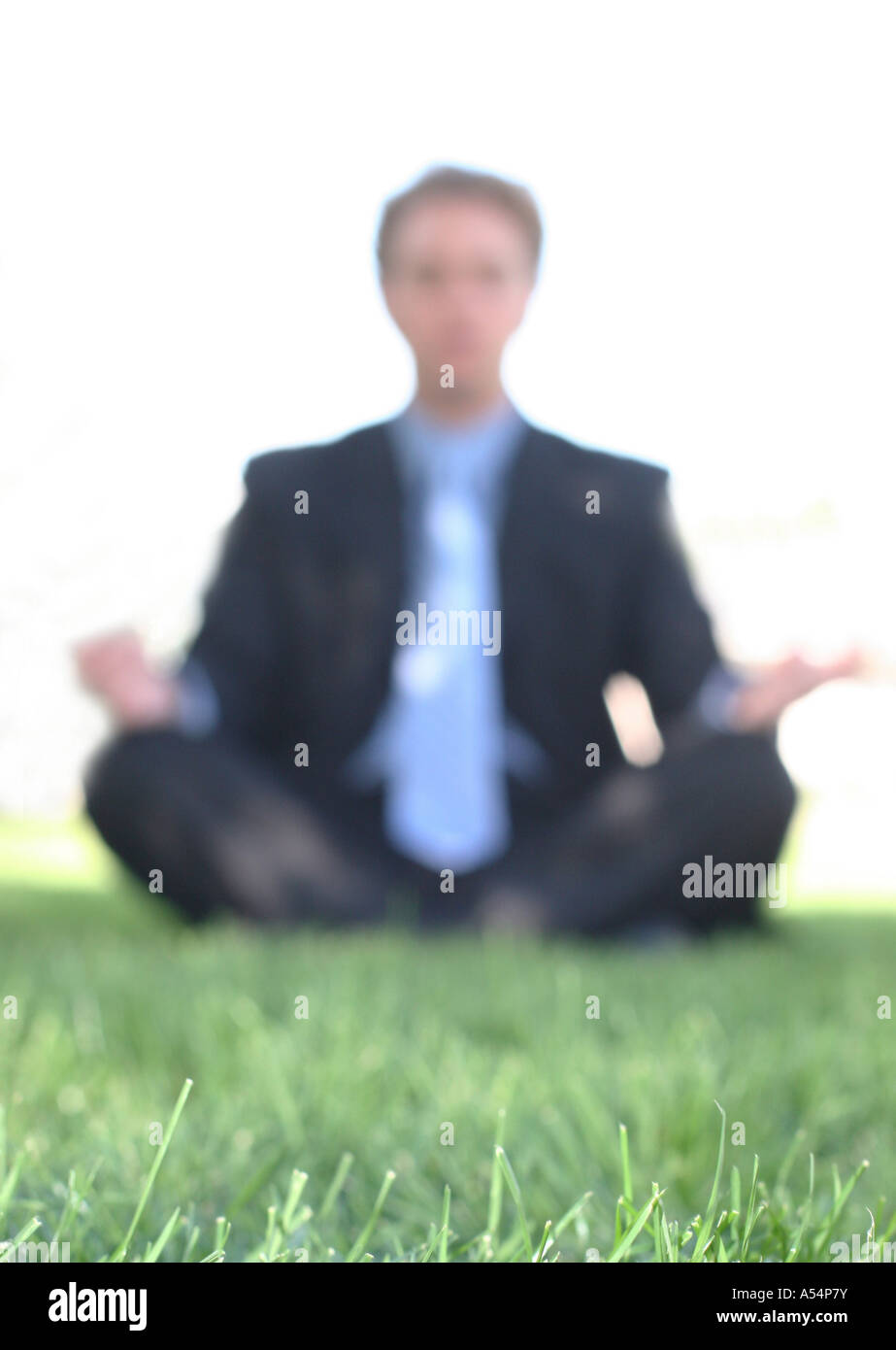 Businessman in black suit is meditating in the green grass with the sun ...