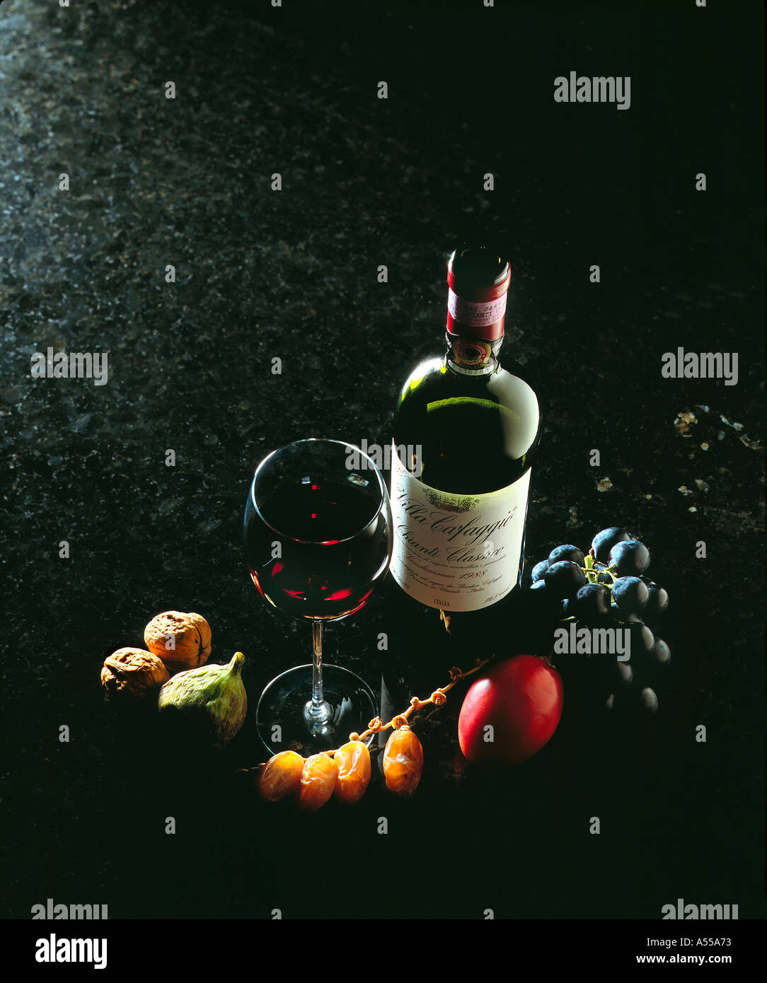 wine bottle chianti classico red wine table glass fruits on dark marble plate Stock Photo