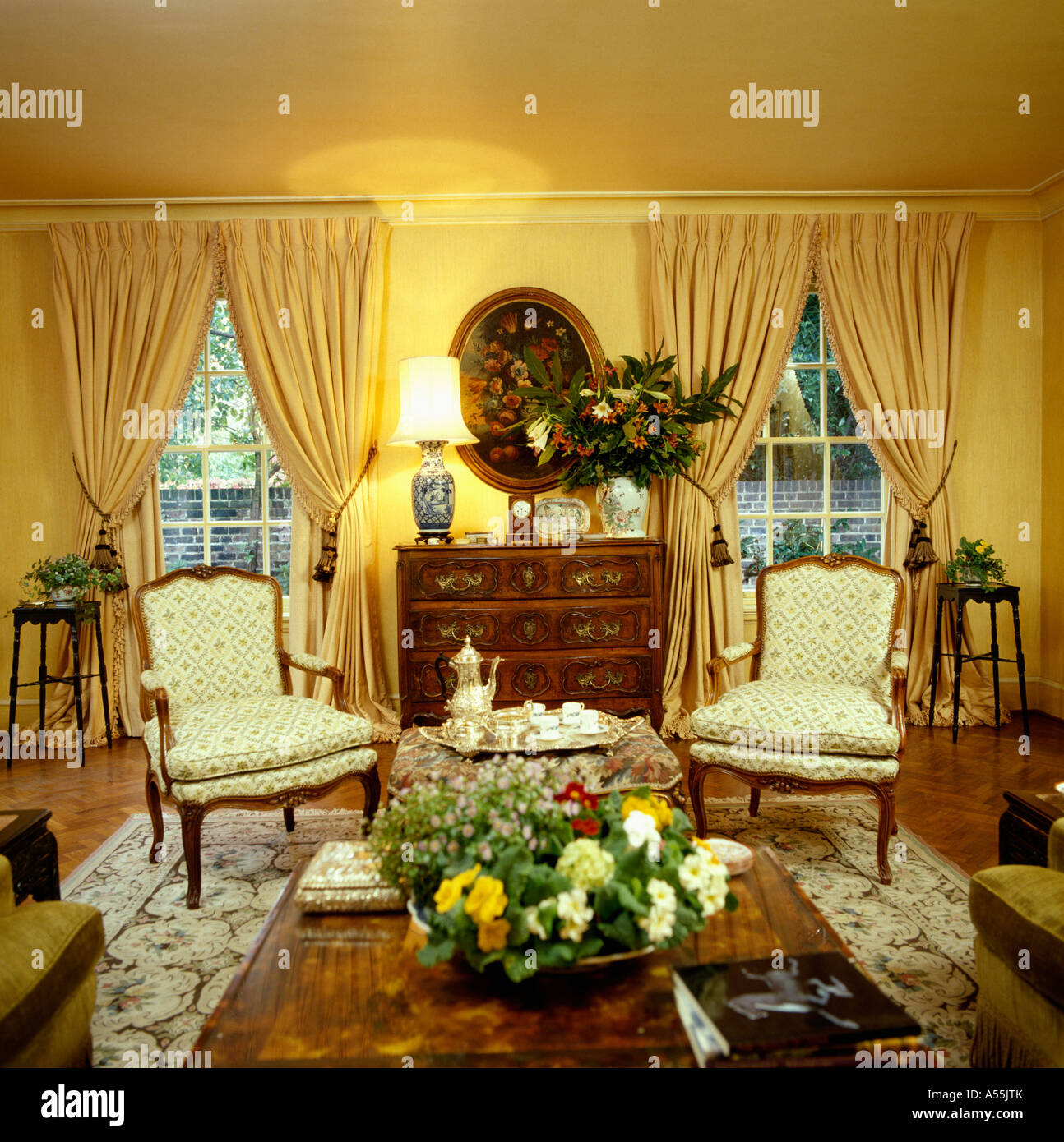 Lighted Lamp On Antique Chest Of Drawers Between Tall Windows With
