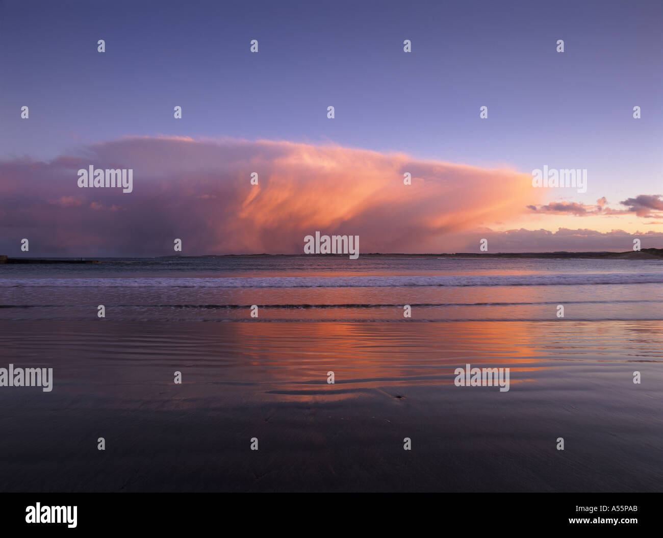 A winter snow storm is coloured by the setting sun over the sea at Beadnell Bay in Northumberland Stock Photo
