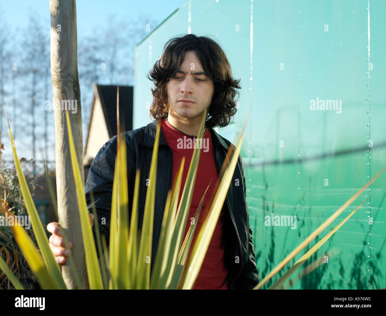 Young man in red and black leather jacket standing amongst a spikey plant Stock Photo