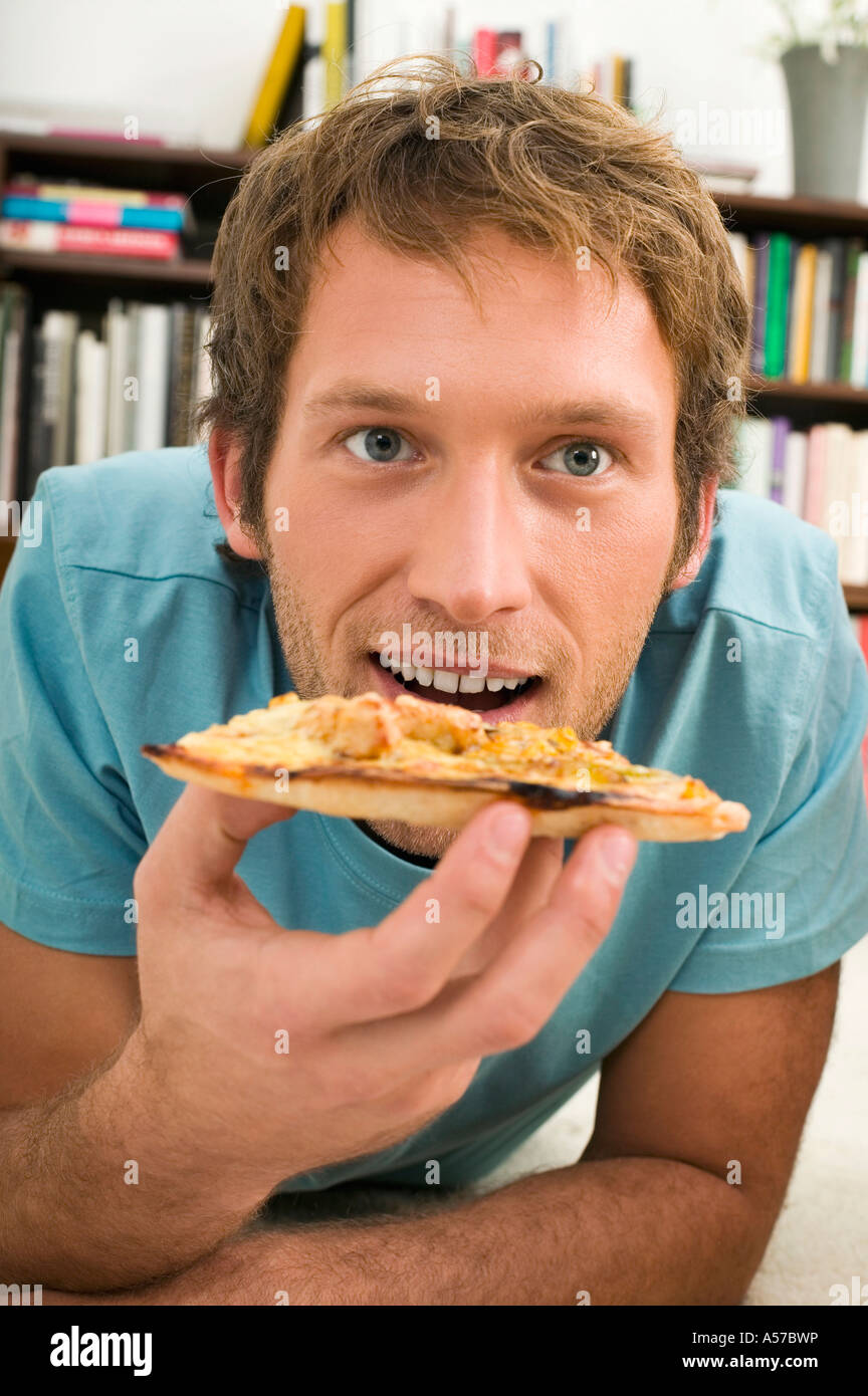 Young man lying on floor, eating pizza, portrait Stock Photo Alamy