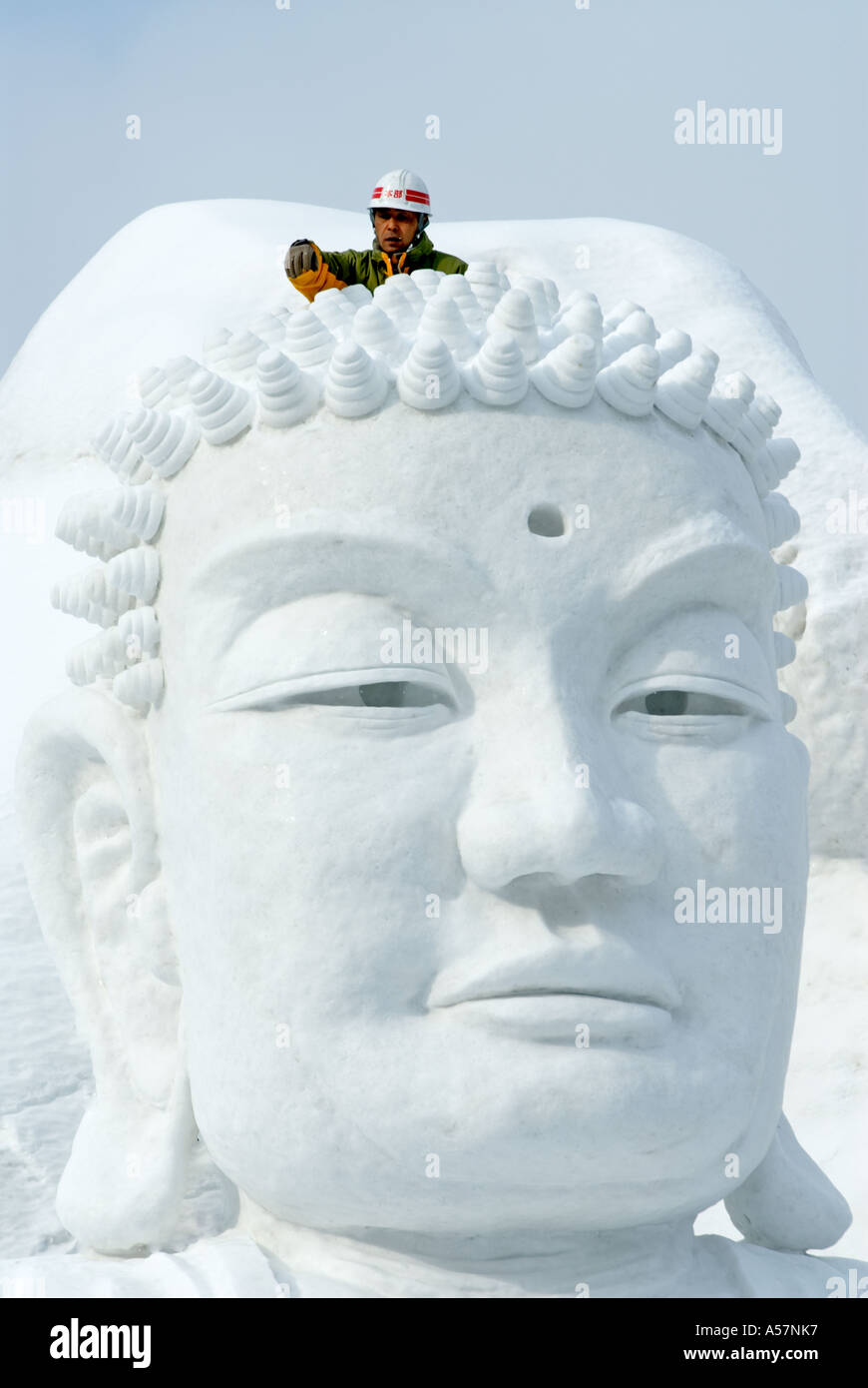 Man clearing snow from head of large Buddha head carved in snow at Sapporo Snow Festival Japan Stock Photo