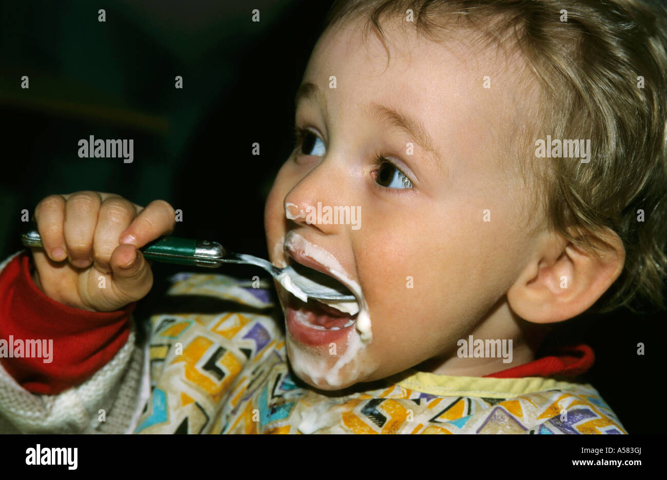 Baby girl eating from a spoon and getting most of it on her face. Stock Photo
