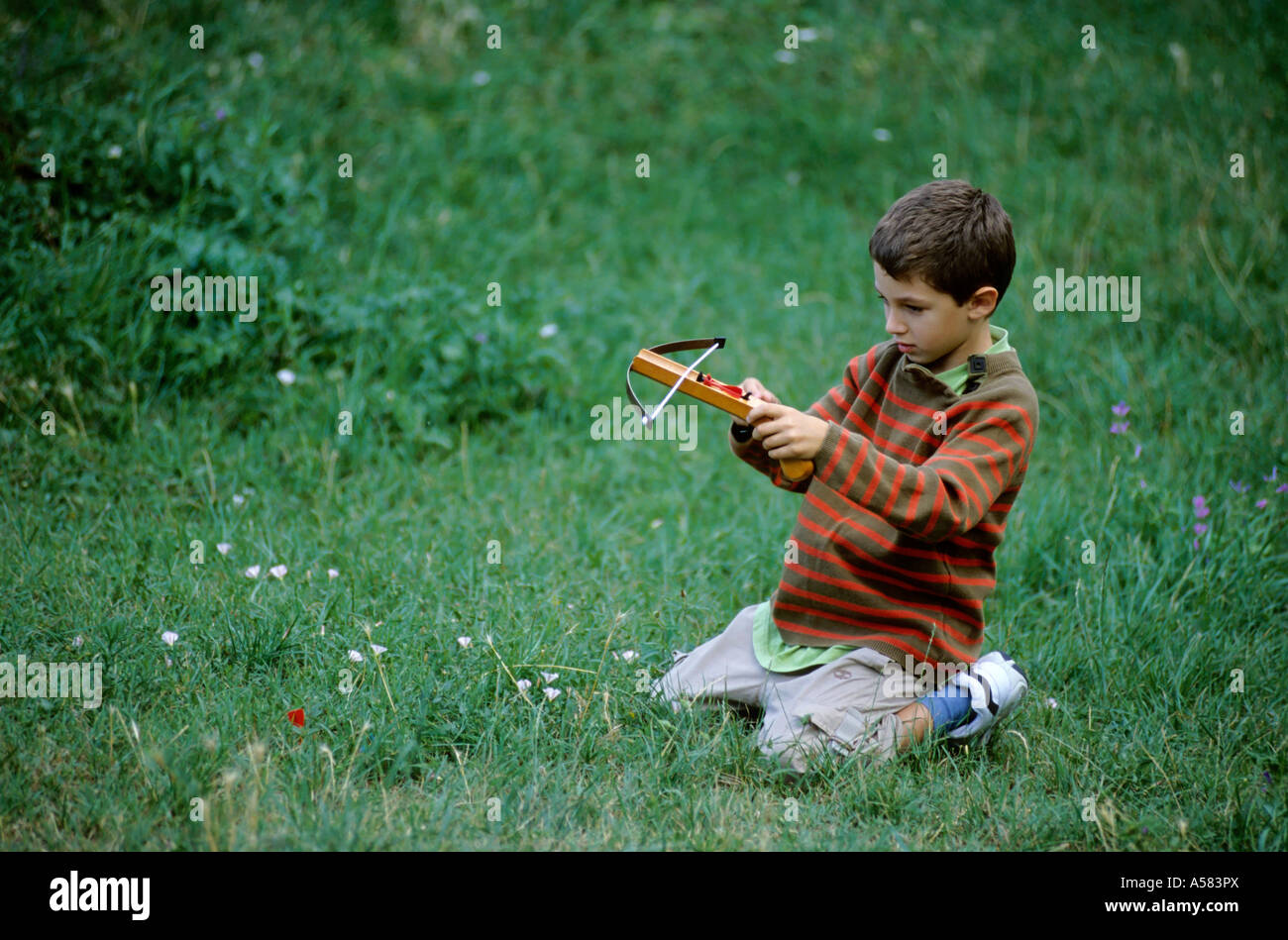 Young boy playing with a crossbow in a grassy field, Provence, France. Stock Photo
