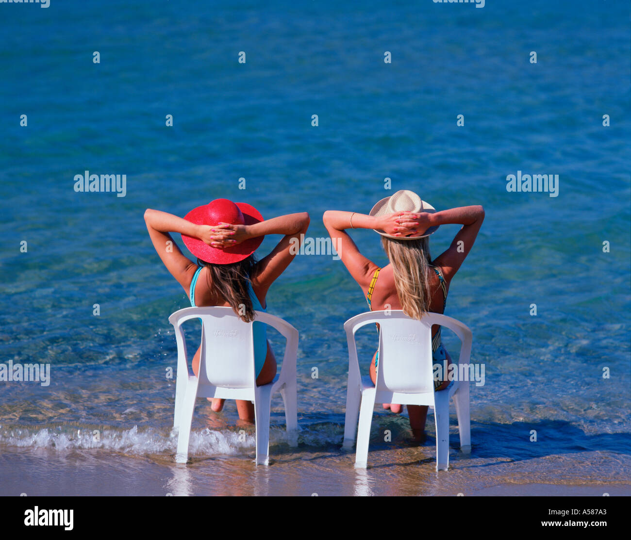 Two young women in summer hats sitting on plastic chairs with their