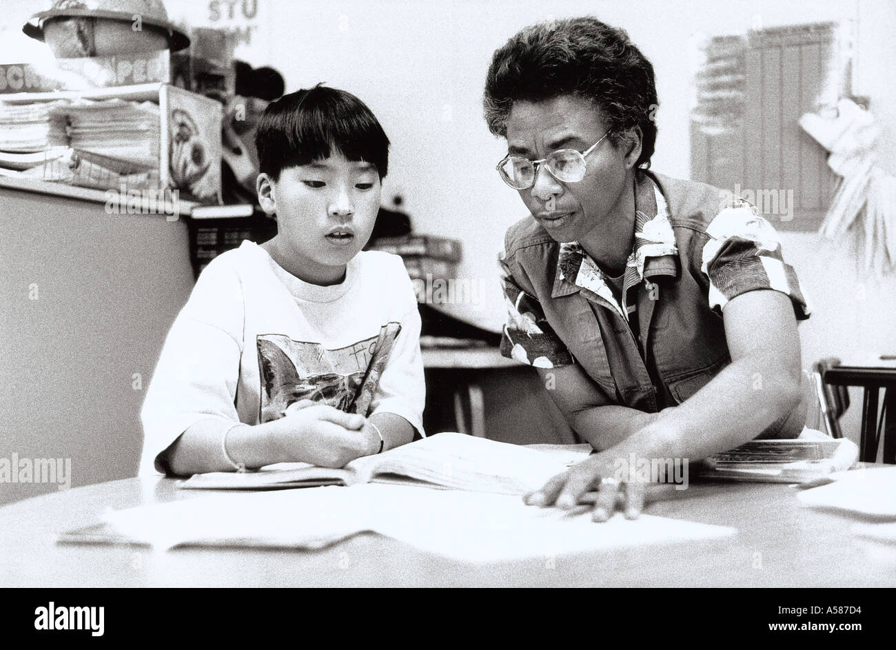 An African Amercian female teacher assisting an Asian fifth grade boy in mathematics Stock Photo