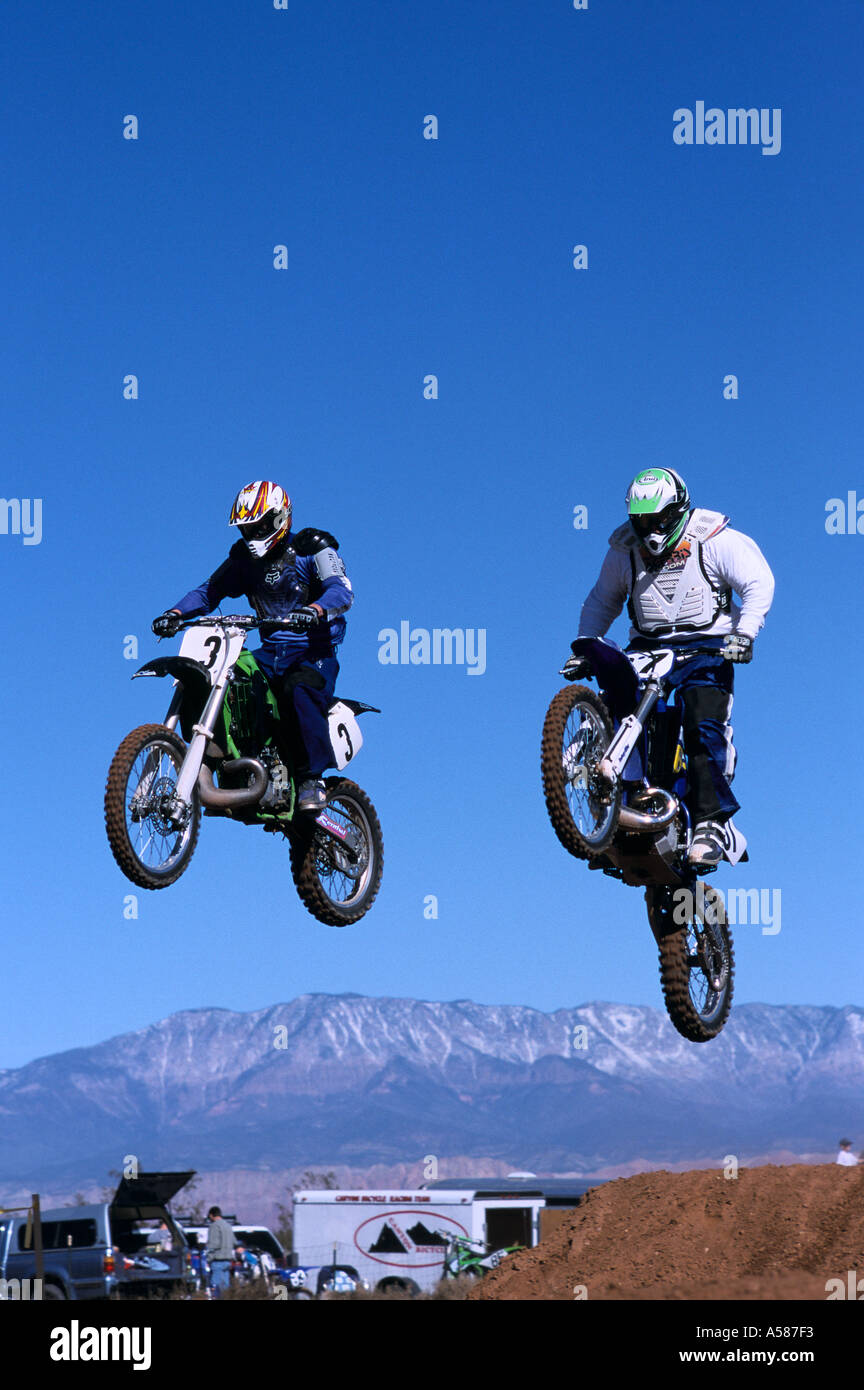 Pair of dirt bike motorcyclists in mid air leaping embankment during