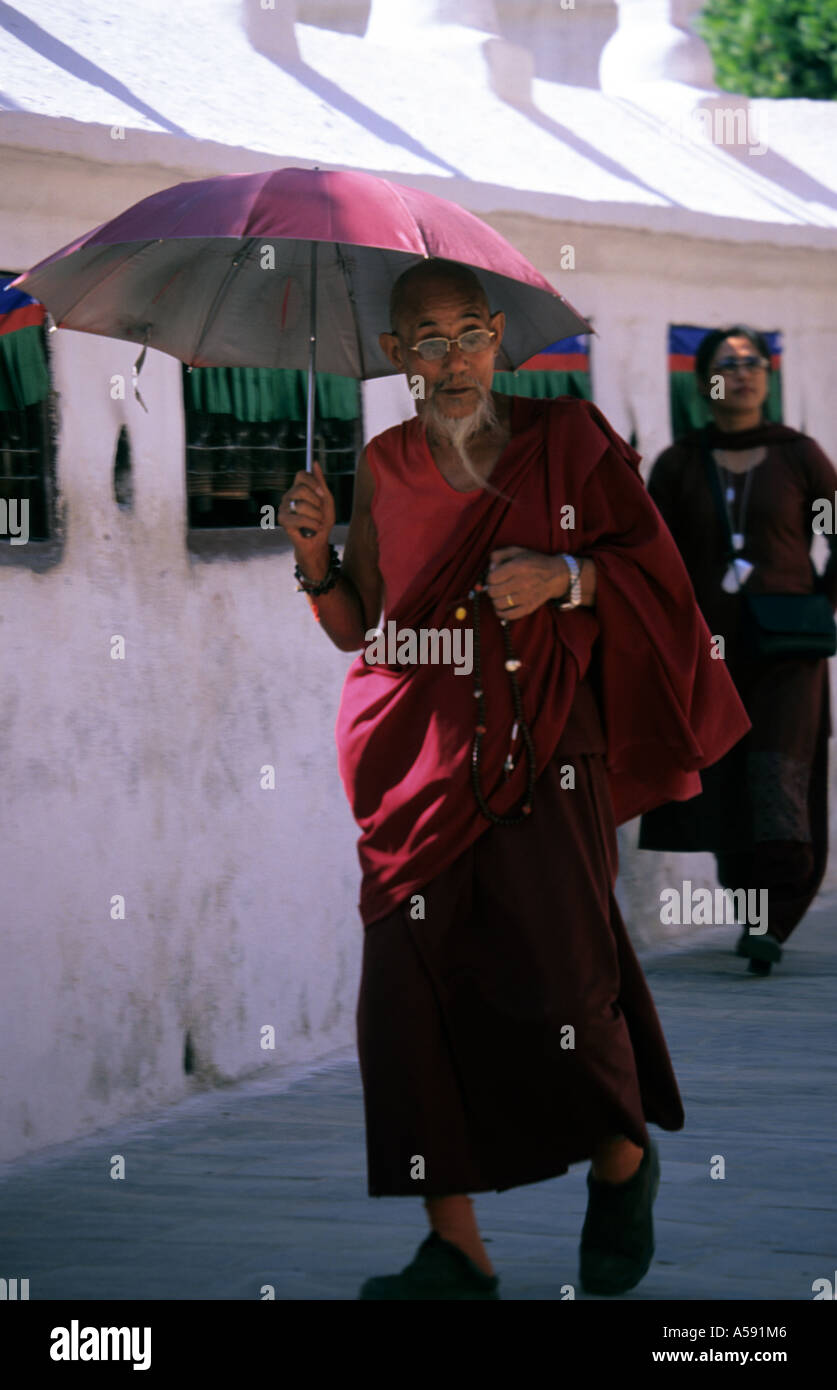 Pilgrim holding umbrella walking around Buddhist Stupa of Bodhnath Kathmandu Nepal Stock Photo