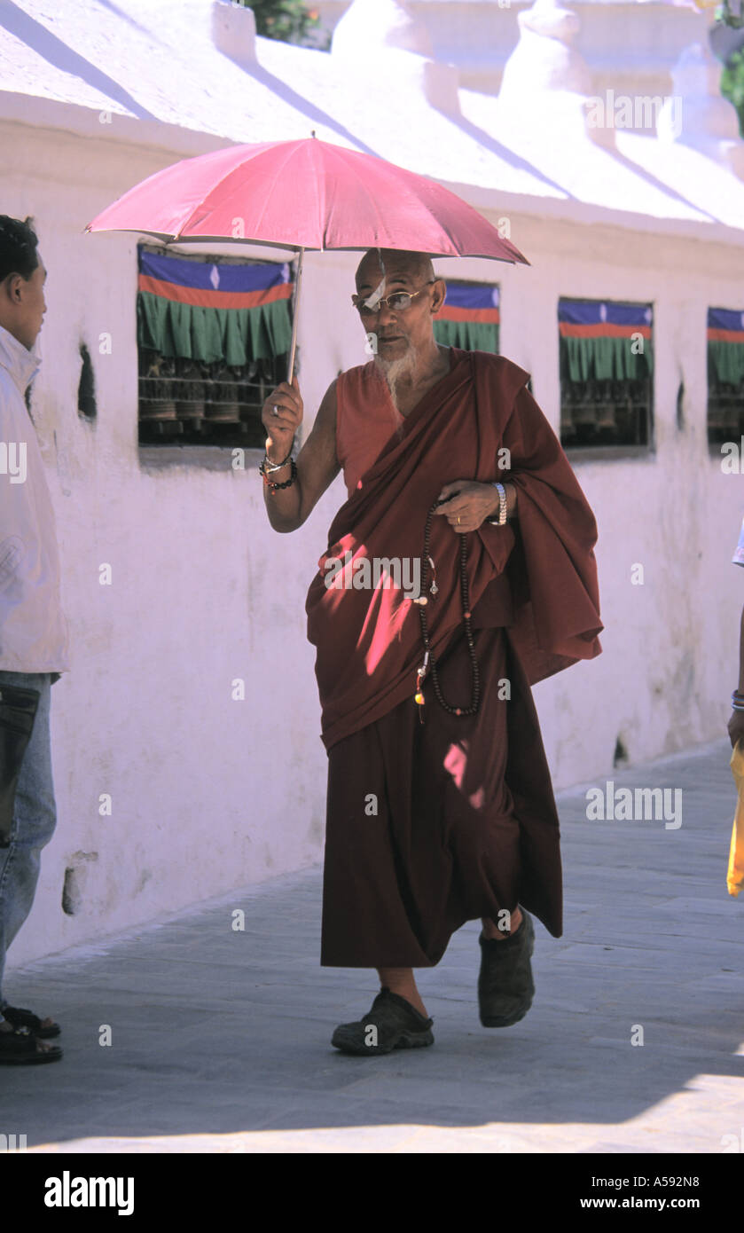 Pilgrim holding umbrella walking around Buddhist Stupa of Bodhnath Kathmandu Nepal Stock Photo