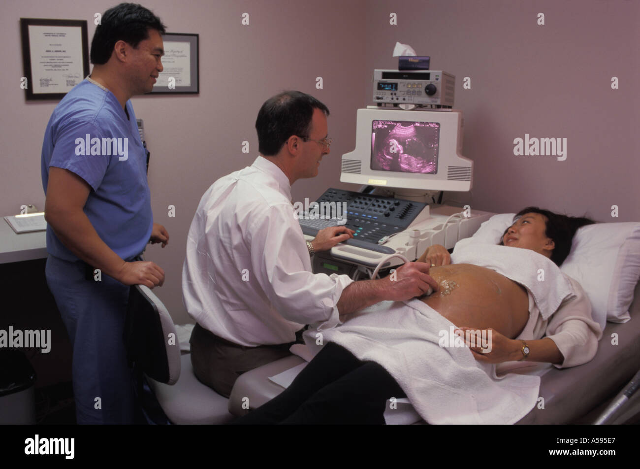 Two doctors performing ultrasound test on Asian woman with five month fetus on monitor Stock Photo