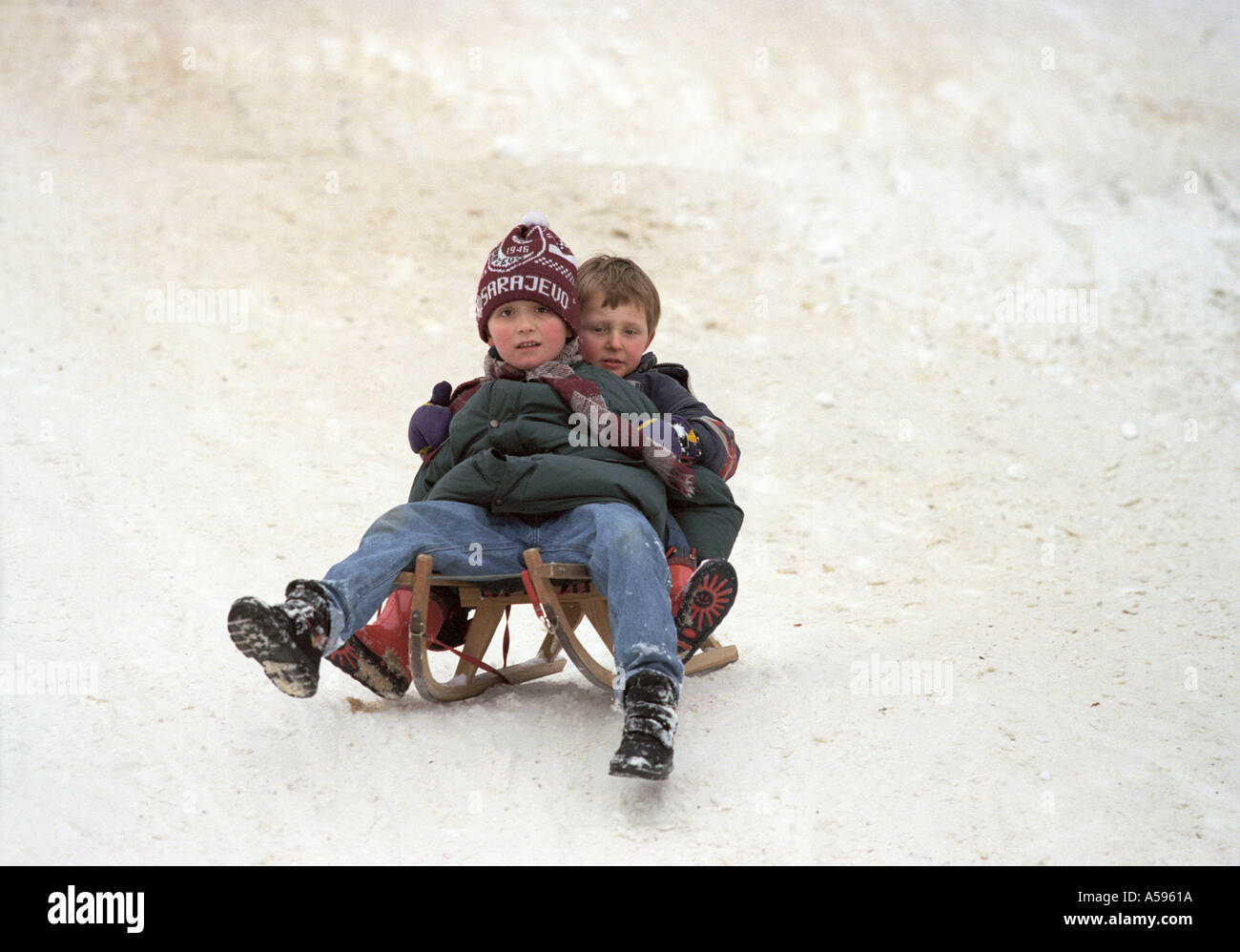 Two boys share a sled in the snow in Sarajevo, Bosnia, site of the 1984 Winter Olympics Stock Photo