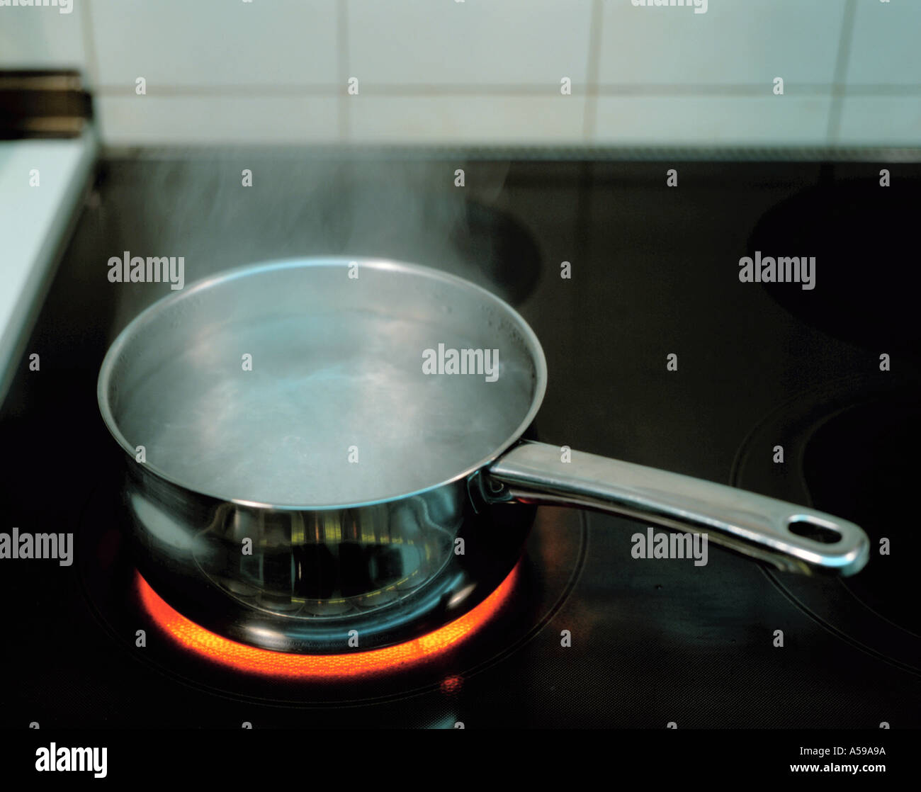 Water boiling in a stainless steel saucepan on an electric halogen hob. Stock Photo