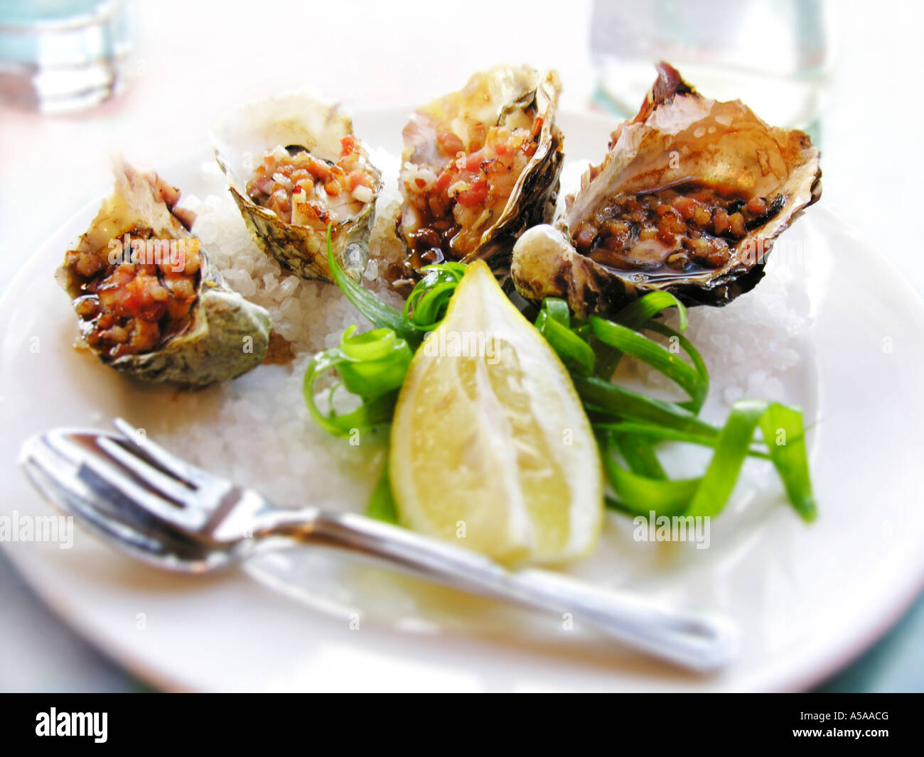 Oysters Kilpatrick on sea salt with lemon and garnish Stock Photo