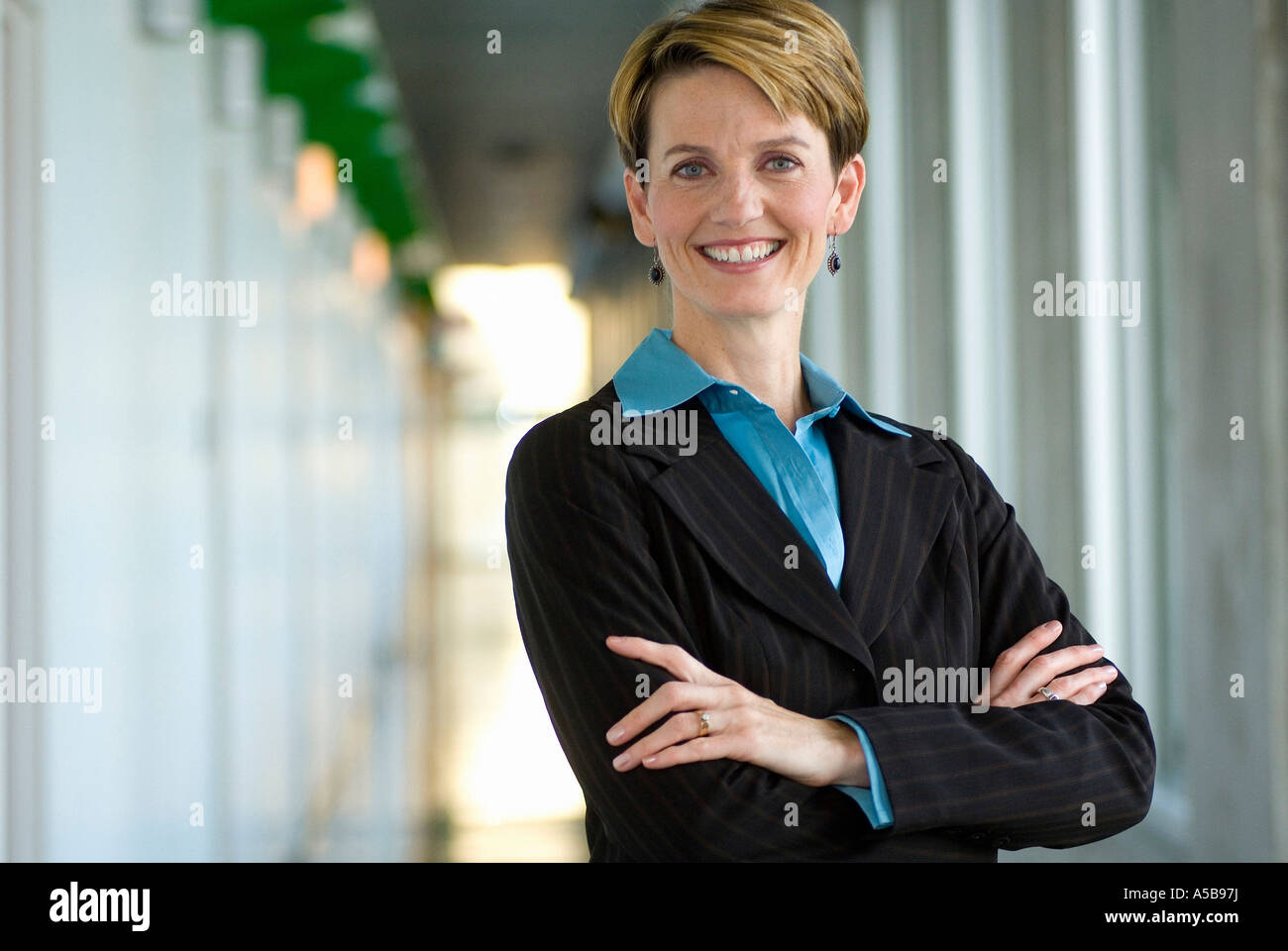 Professional female business executive folding arms while standing in office hallway. Stock Photo