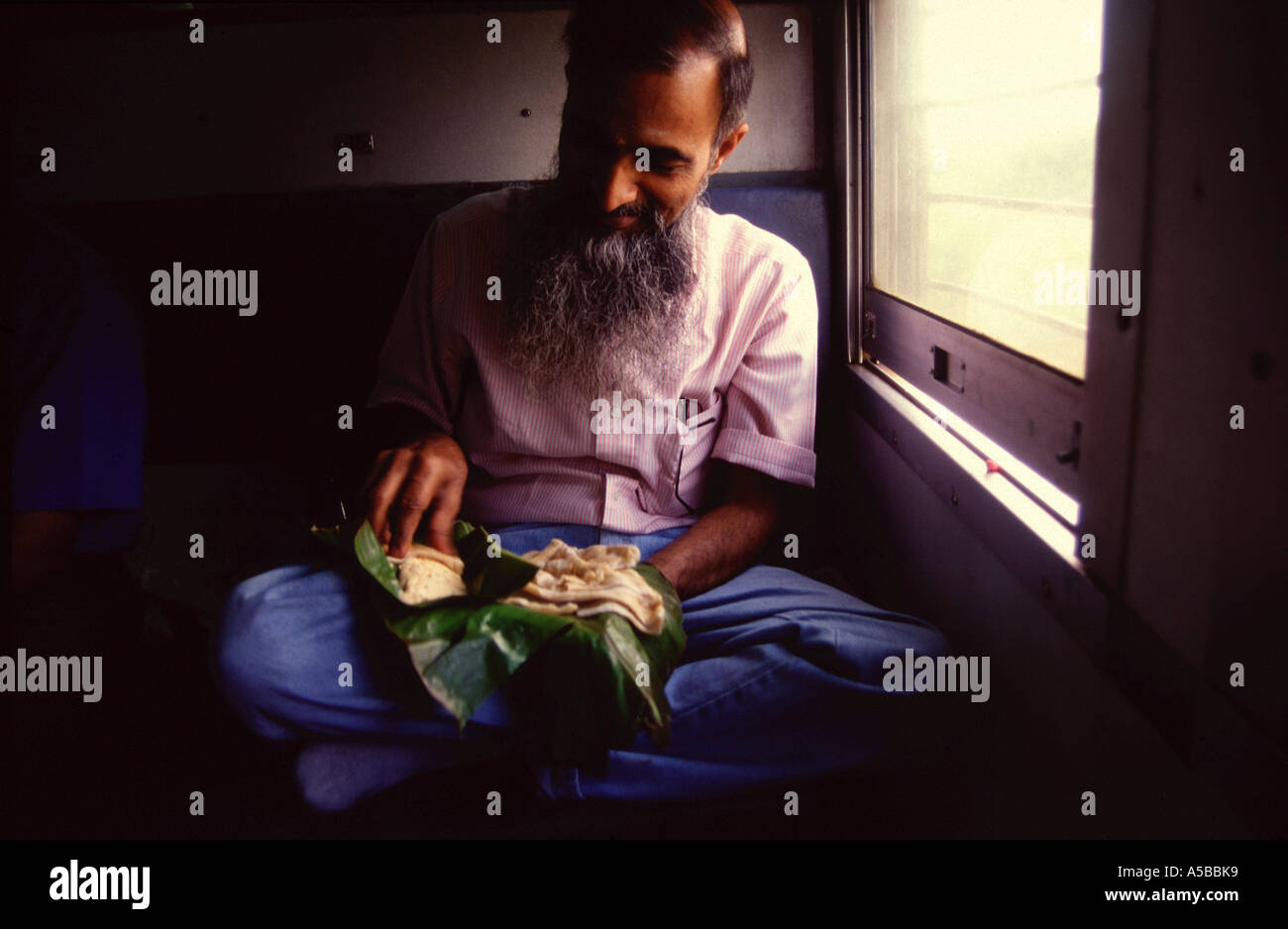 An Indian commuter sits crossed legs and eats South Indian Thali meal on banana leaf with his hands in a train Tamil Nadu state South India Stock Photo