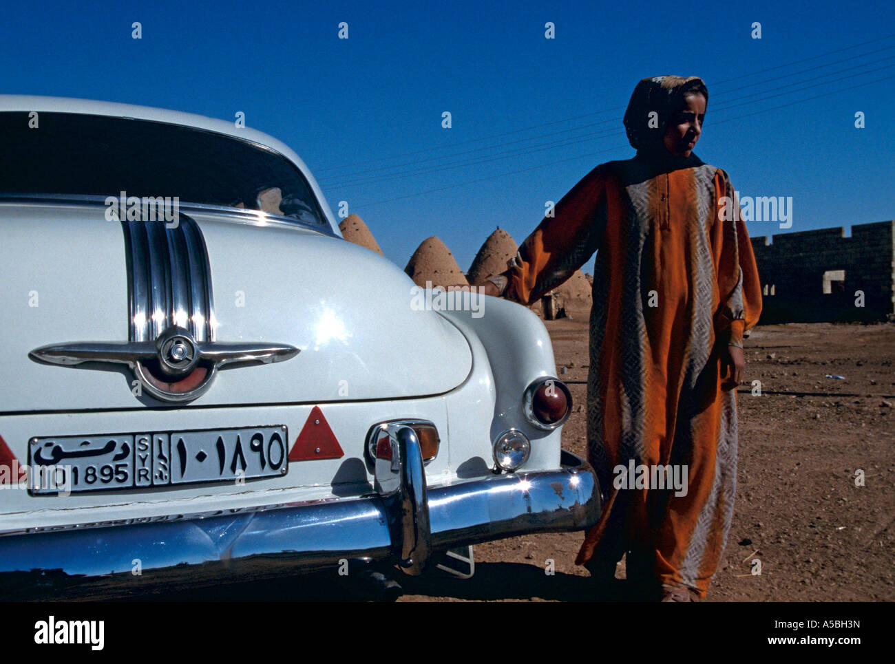 A Syrian woman standing beside a white Cadillac with beehive houses visible in the background Stock Photo