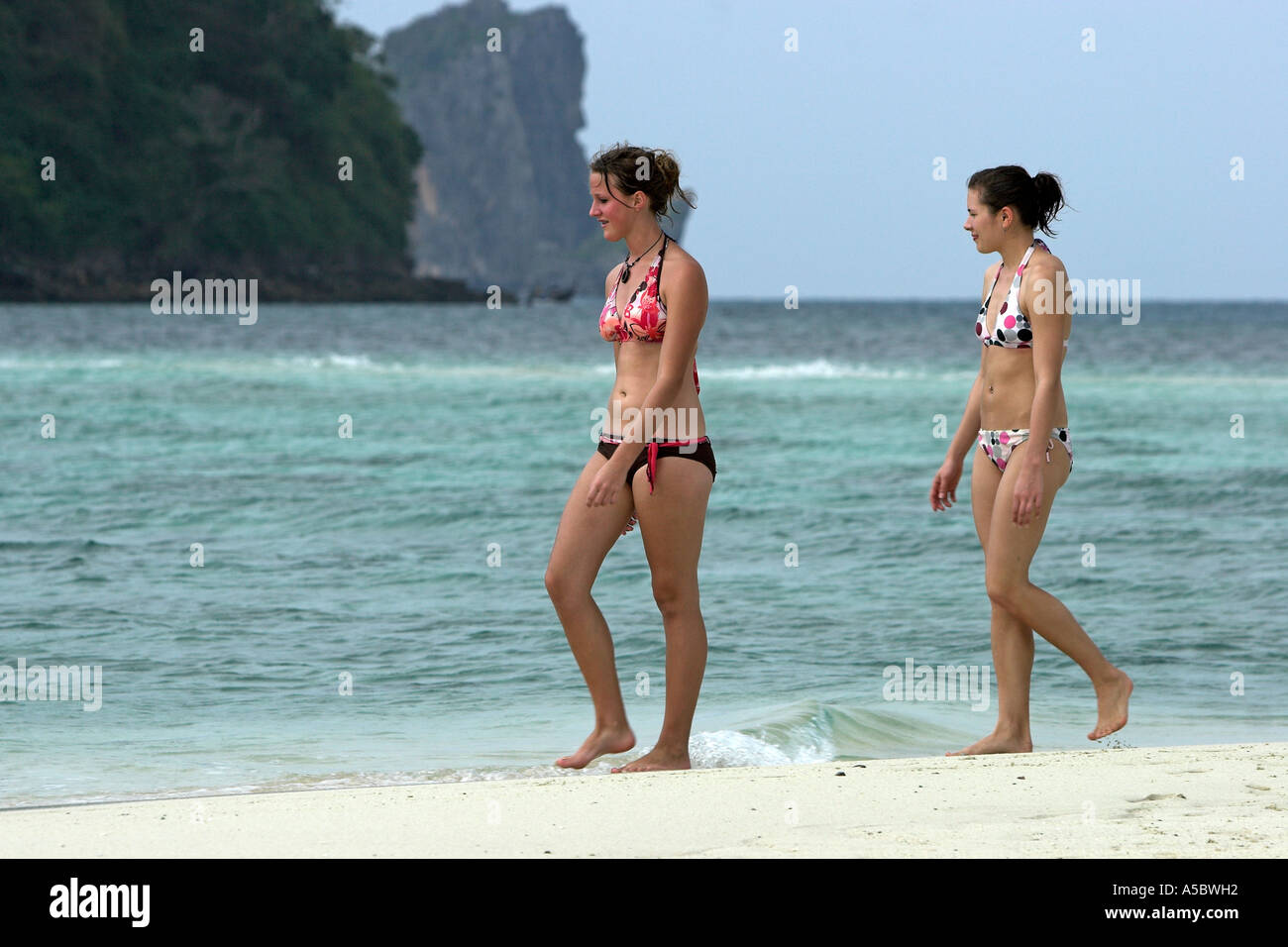 Two young women in bikinis walk along white sand beach Ko Tup island Thailand Stock Photo