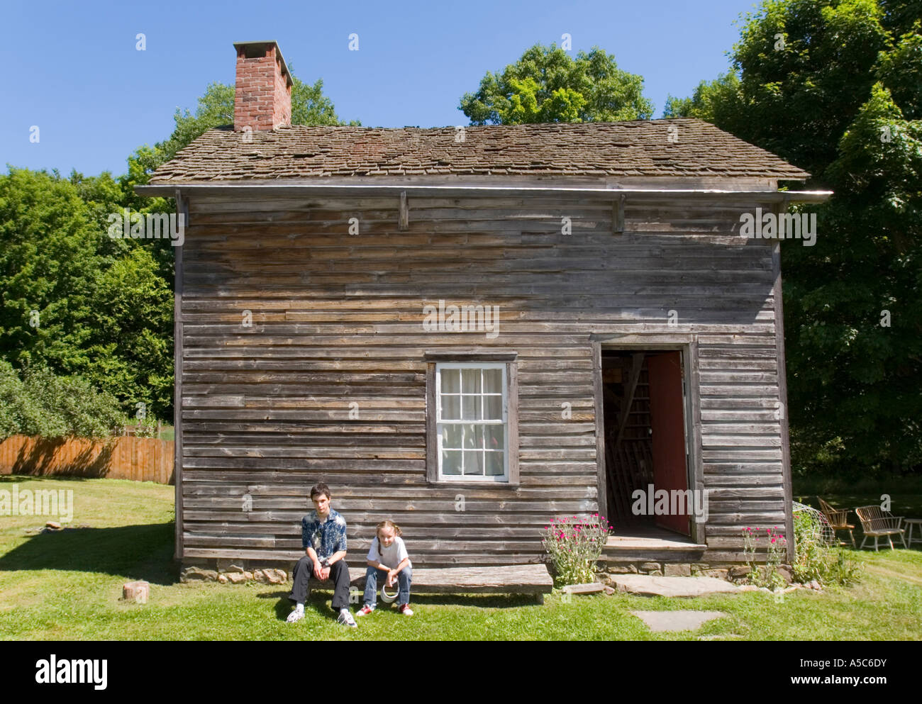 Two teenagers sitting on a bench in front of an old wooden house Stock ...