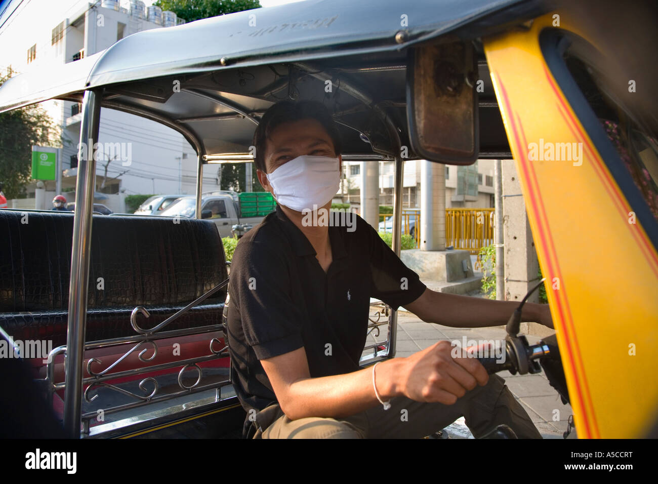 Smog protection in the busy capital city of Bankok,Thailand.  Driver of Tuk-tuks taxi wearing pollution filter mask filtering vehicle exhaust fumes. Stock Photo