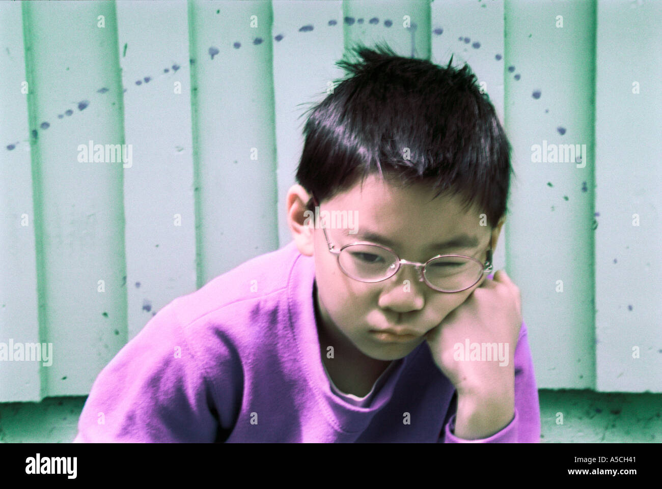 An odd color horizontal image of a young Asian boy brooding with his head on his fist Stock Photo