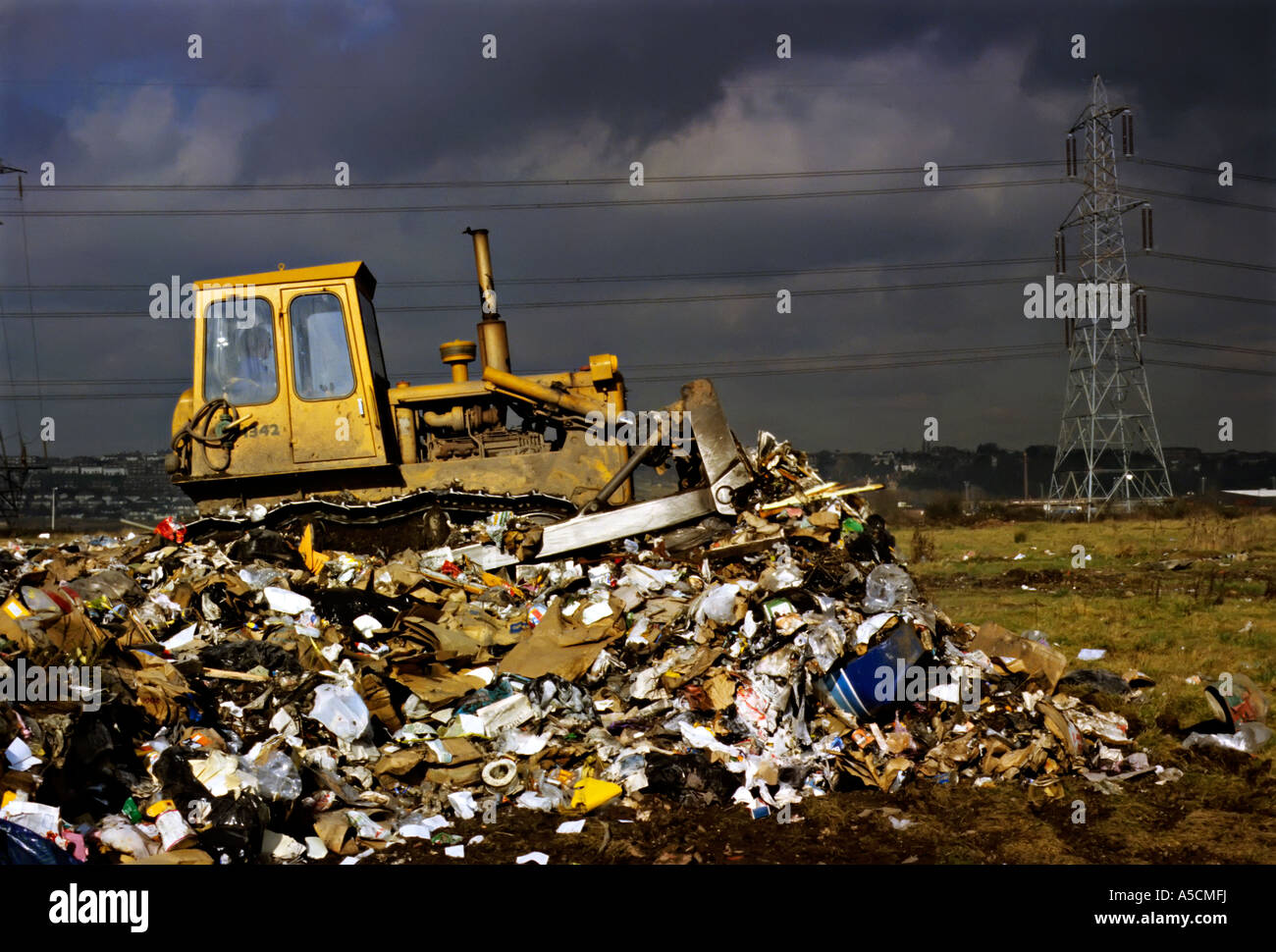 Bulldozing rubbish on landfill site covering new ground with storm clouds gathering Newport Gwent Wales UK Stock Photo