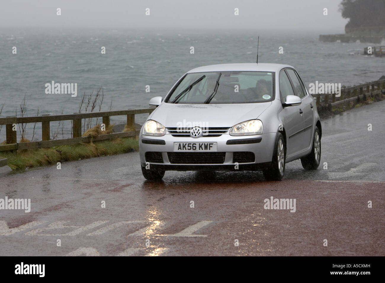 silver vw golf car with headlights and wipers on drives along the coast road on a stormy day Portaferry county down Stock Photo