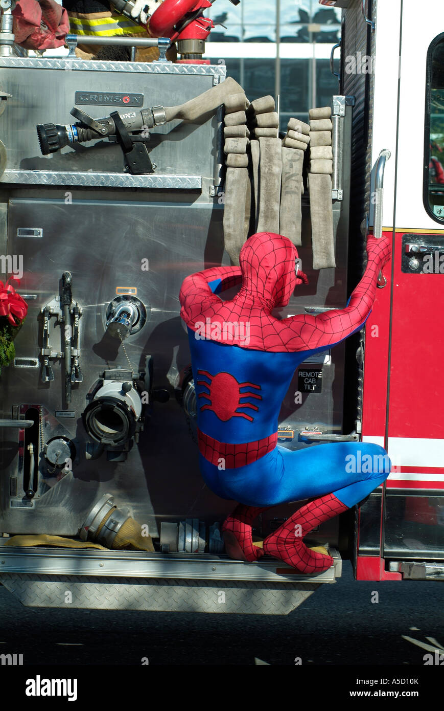 Man wearing a spiderman costume and hanging on a firefight truck Stock Photo