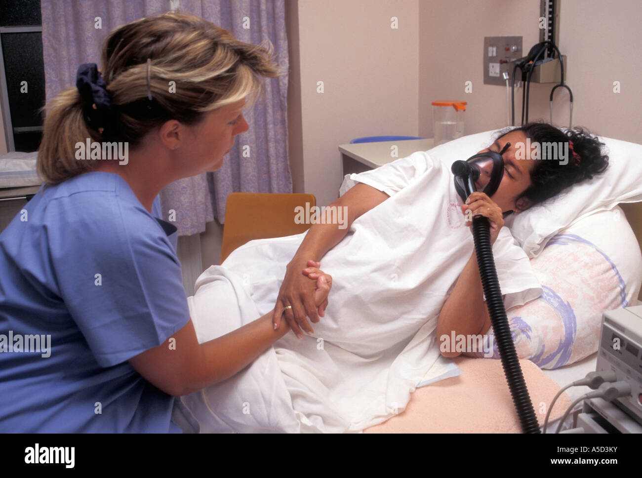 midwife supporting labouring hispanic woman in hospital with gas and air mask Stock Photo