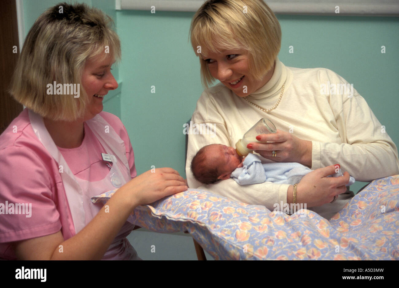 nurse or midwife helping new mother bottlefeed her baby in hospital Stock Photo