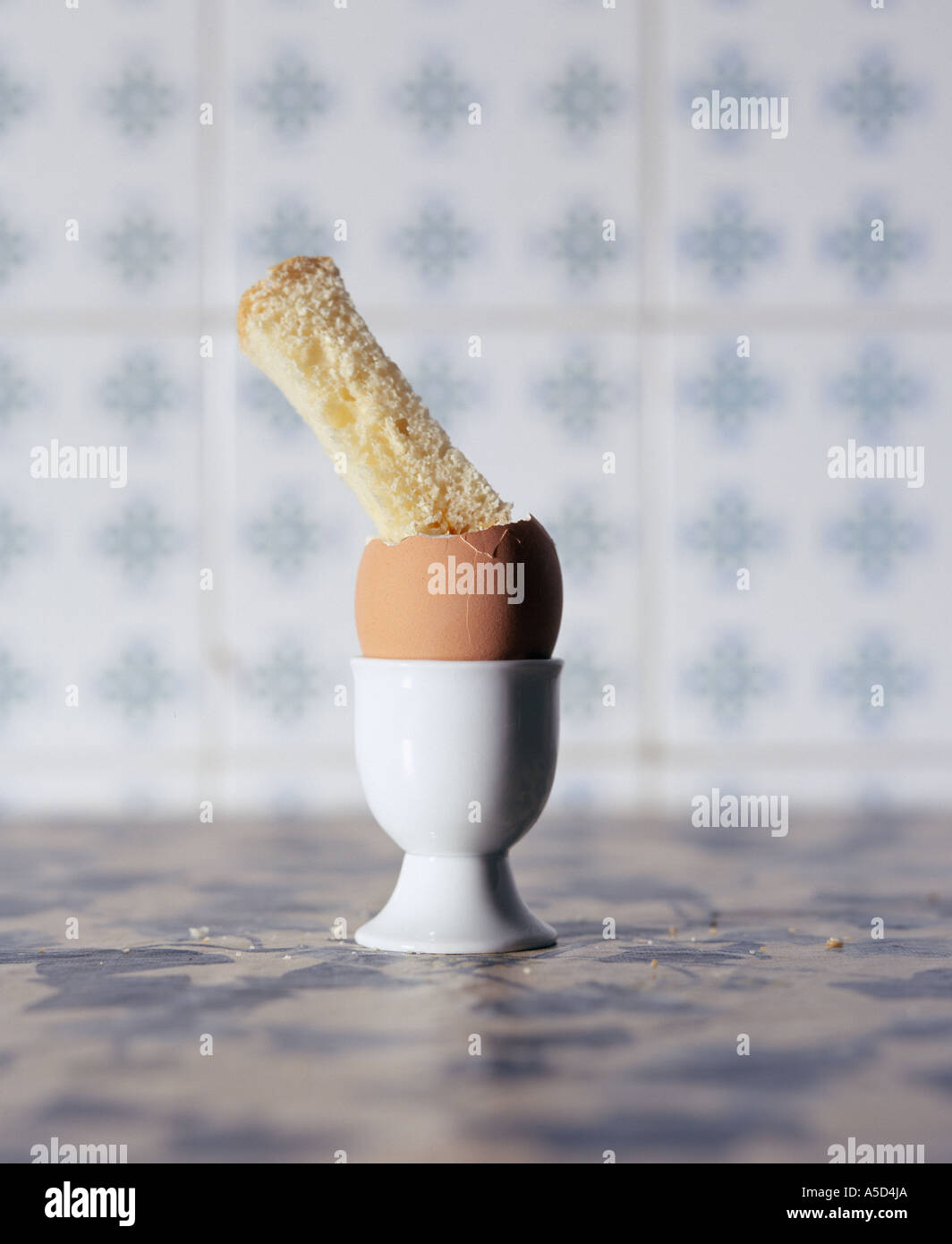 boiled egg and bread soldier against blue tiled background Stock Photo
