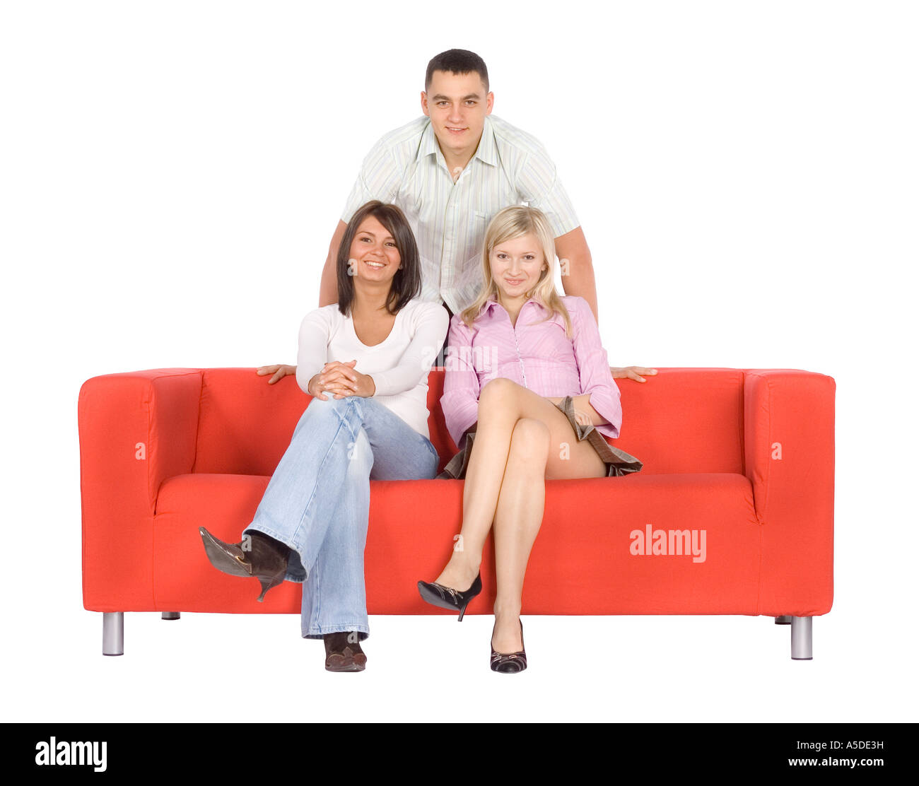 Two women sitting on the orange couch. There's a man standing behind