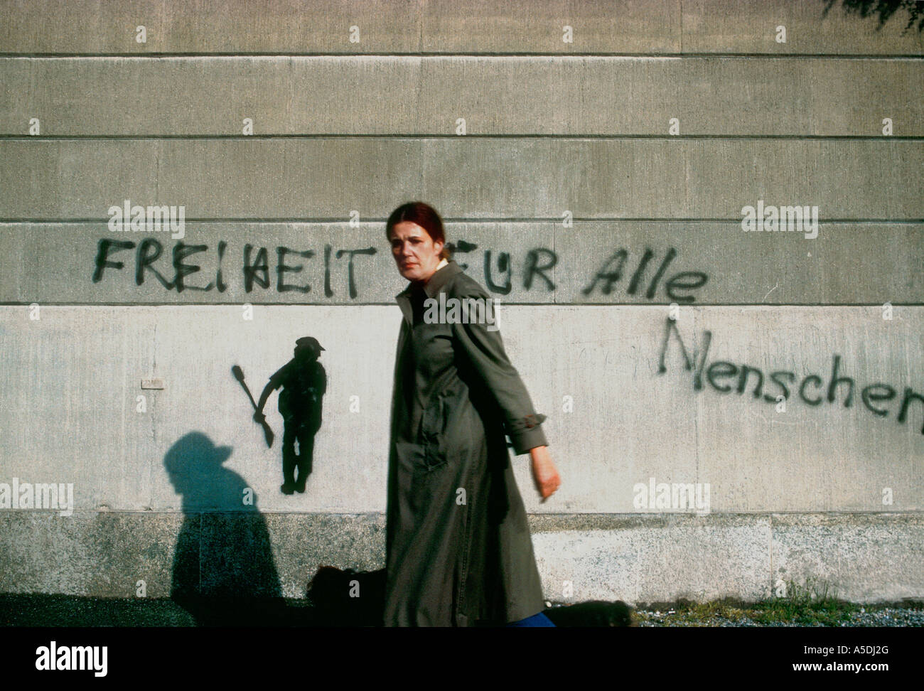 woman in long coat walking past political graffiti on wall in Zurich, Switzerland Stock Photo