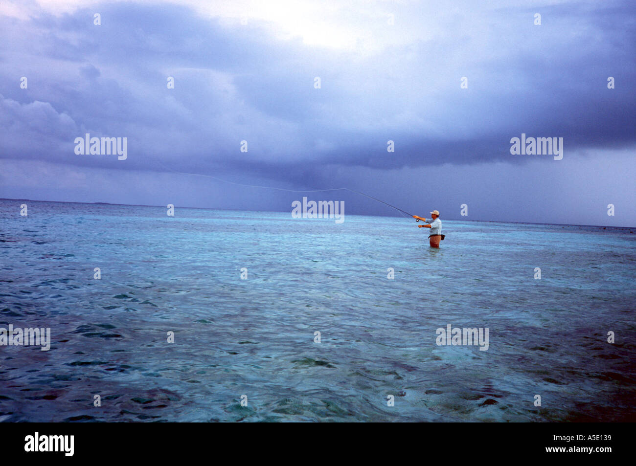 Fly fisherman fishing on a shallow flat in southern Belize with storm clouds in the background Central America Caribbean Stock Photo