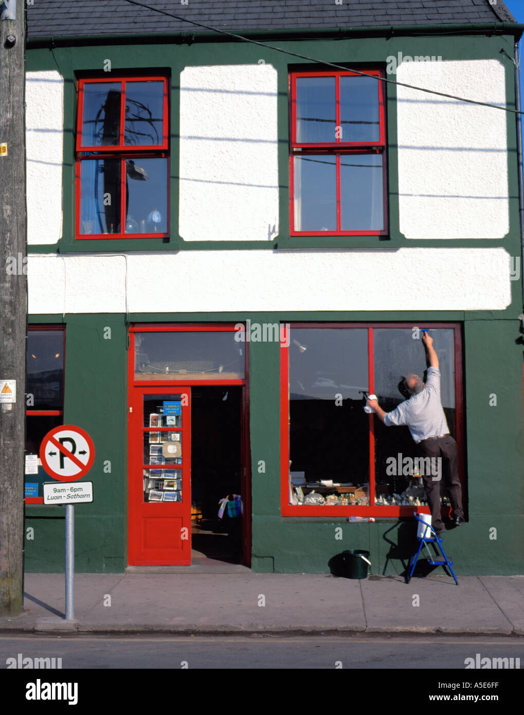 Man cleaning a shop window, Dingle village, Dingle Peninsula, County Kerry, Eire (Ireland). Stock Photo