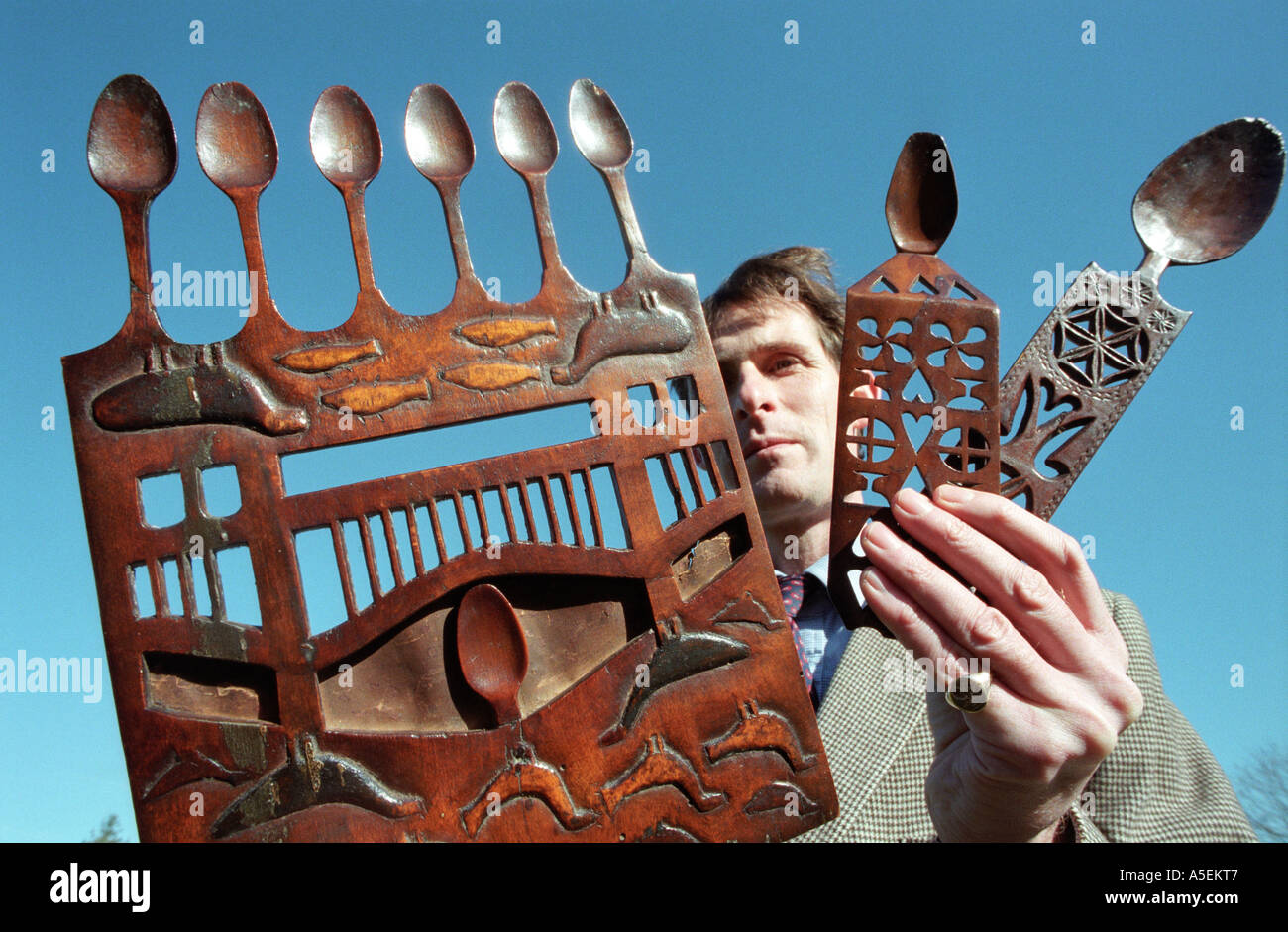 Young man holding three antique carved wood love spoons from Wales at