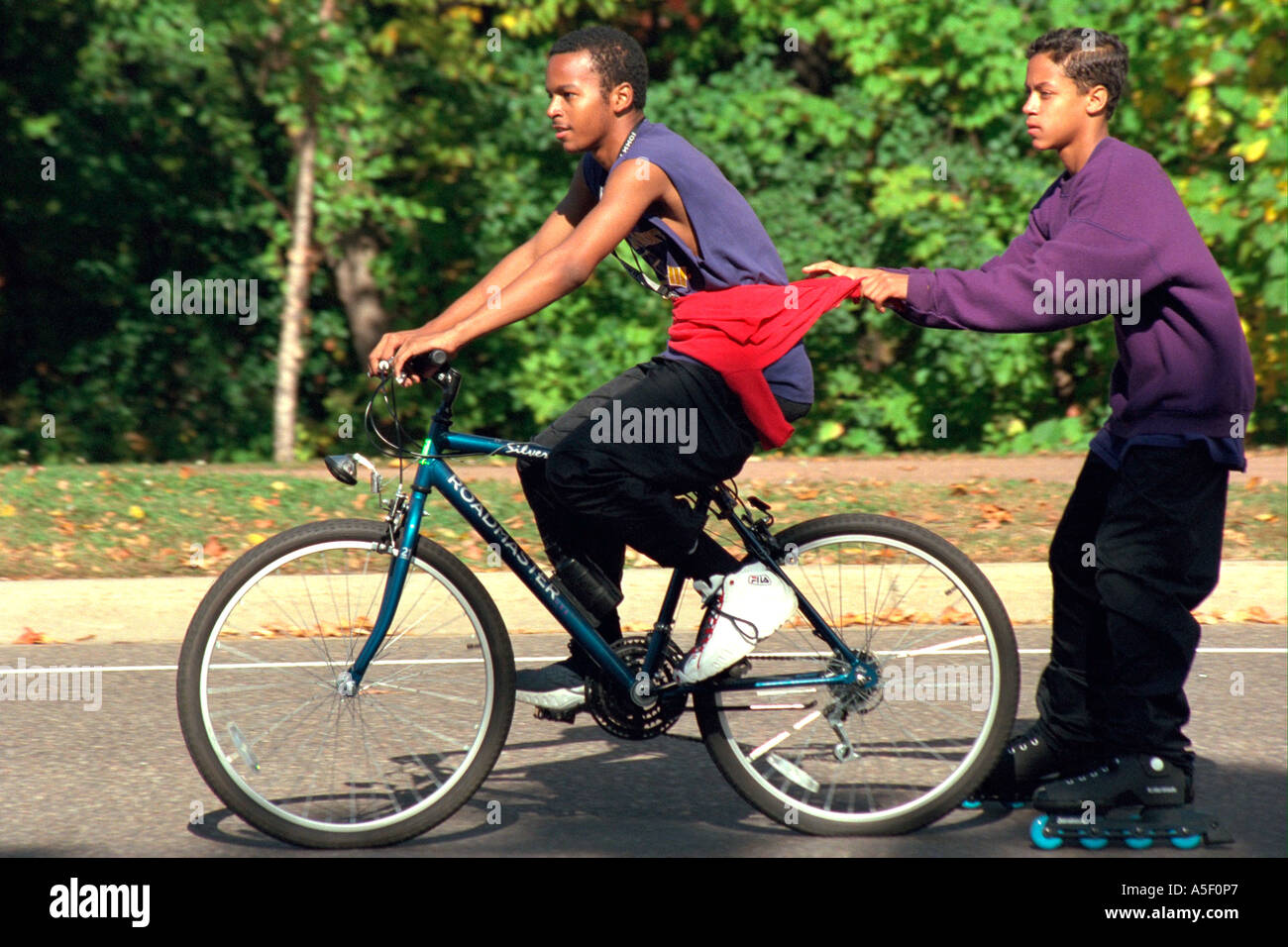 Friend hitching ride behind bicycle on rollerblades age 15. St Paul  Minnesota USA Stock Photo - Alamy