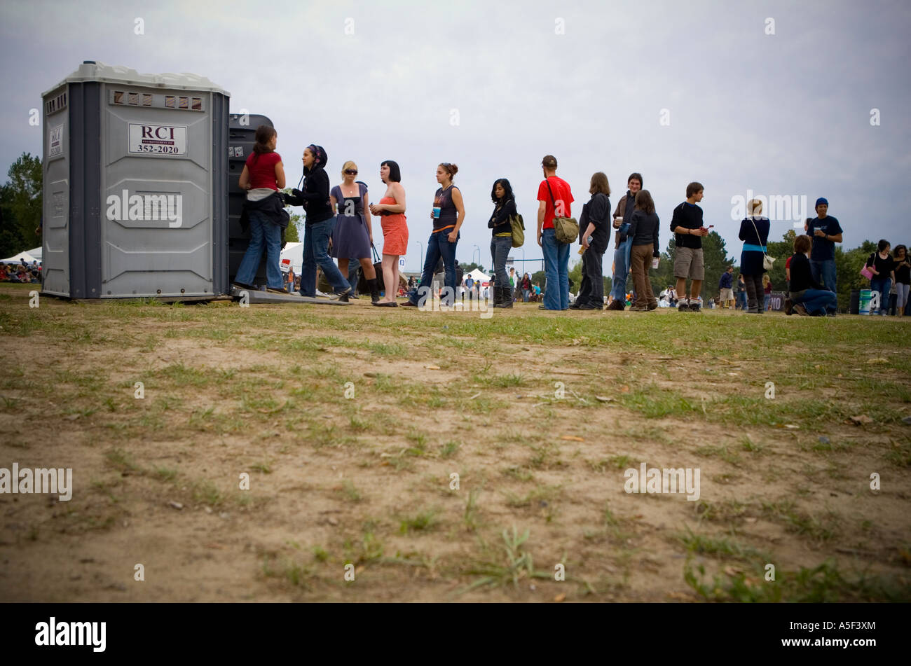 A queue of people waiting to use an outdoor chemical toilet Stock Photo