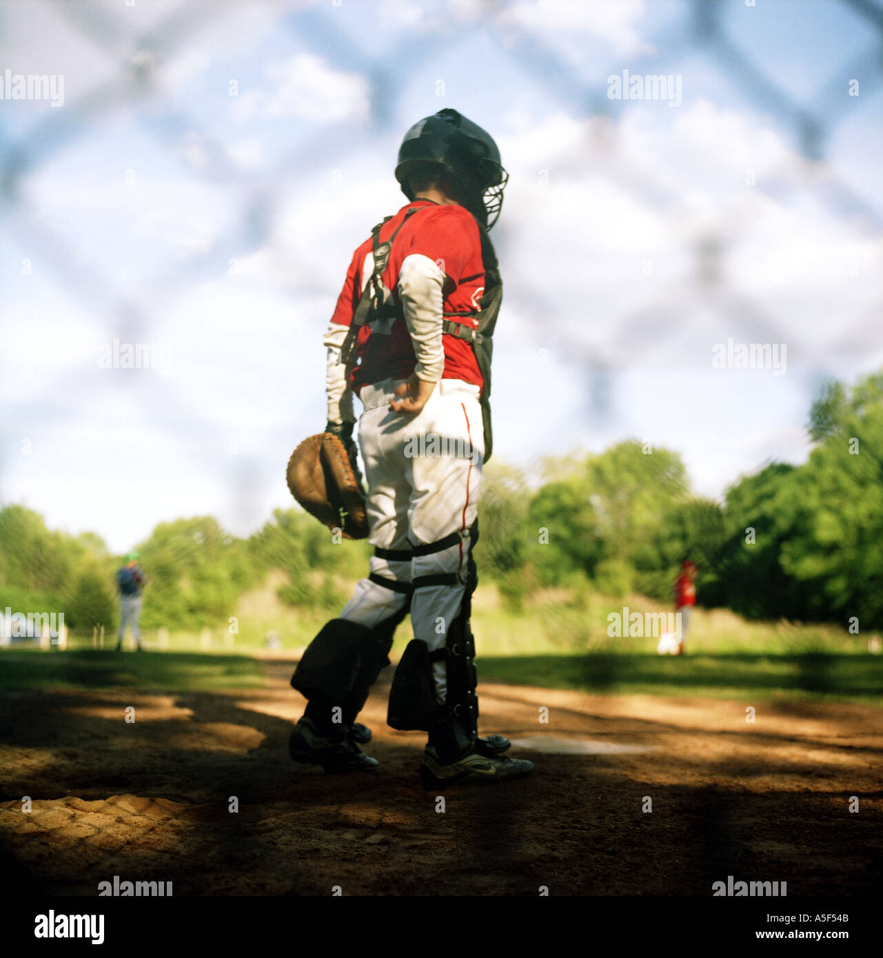 Boy wearing catchers uniform on a baseball field behind a fence Stock Photo